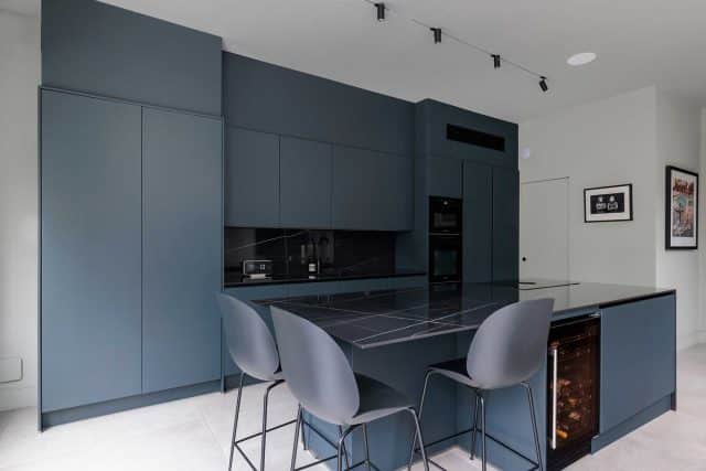 Modern kitchen design featuring dark cabinetry and a sleek island, with an Arch KBB team member present. The space showcases a contemporary aesthetic, including integrated appliances and minimalist decor. Ideal for those seeking inspiration for stylish kitchen renovations.