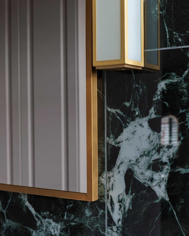 Close-up view of a modern kitchen featuring a striking black marble splashback with white veining, complemented by sleek gold accents and a stylish light fixture. An Arch KBB team member is present, showcasing the design elements in a contemporary setting.