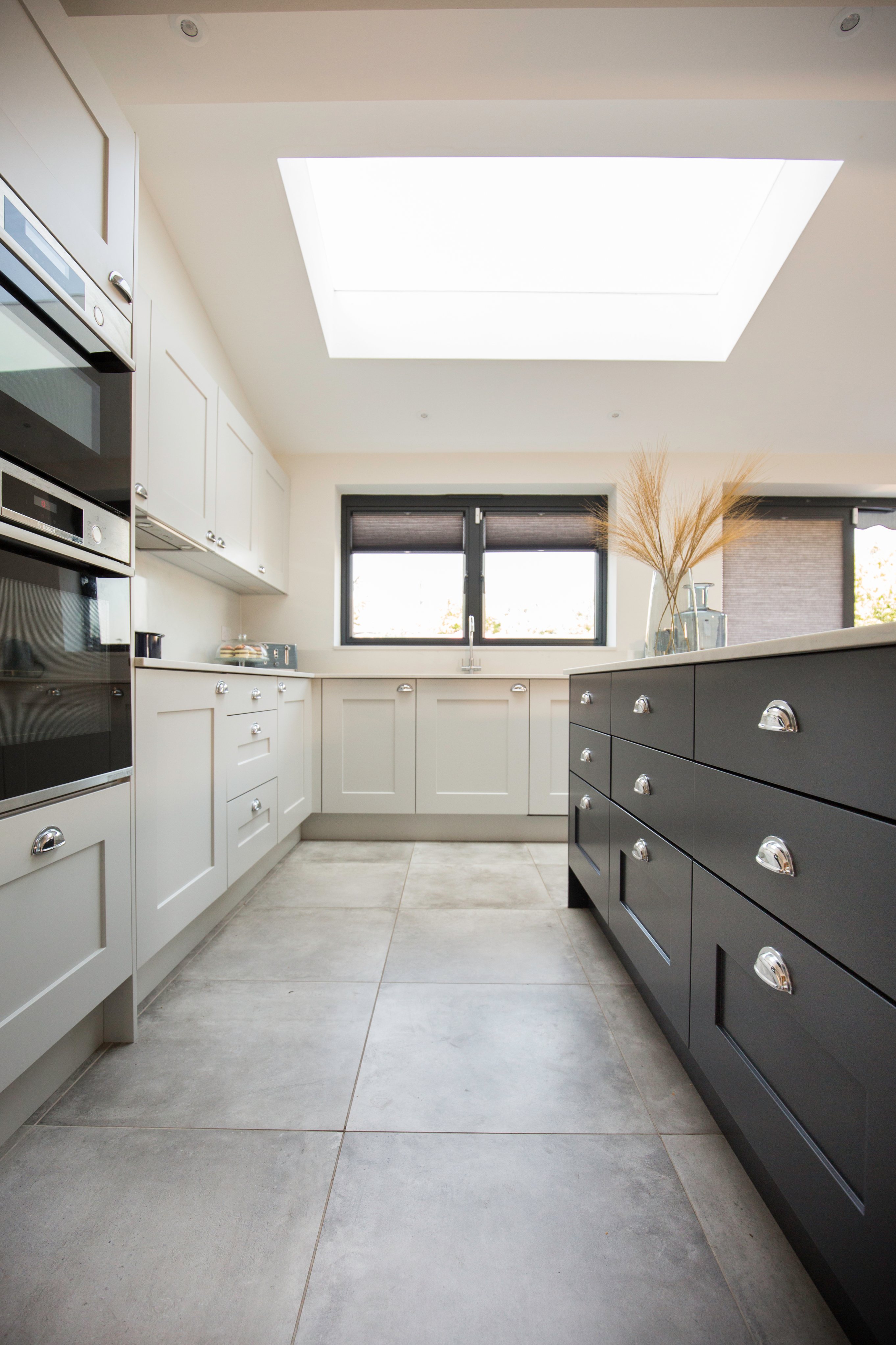 Modern kitchen interior featuring a combination of grey and white cabinetry, a skylight for natural lighting, and decorative elements. An Arch KBB team member is present, showcasing a stylish and functional design ideal for contemporary homes.
