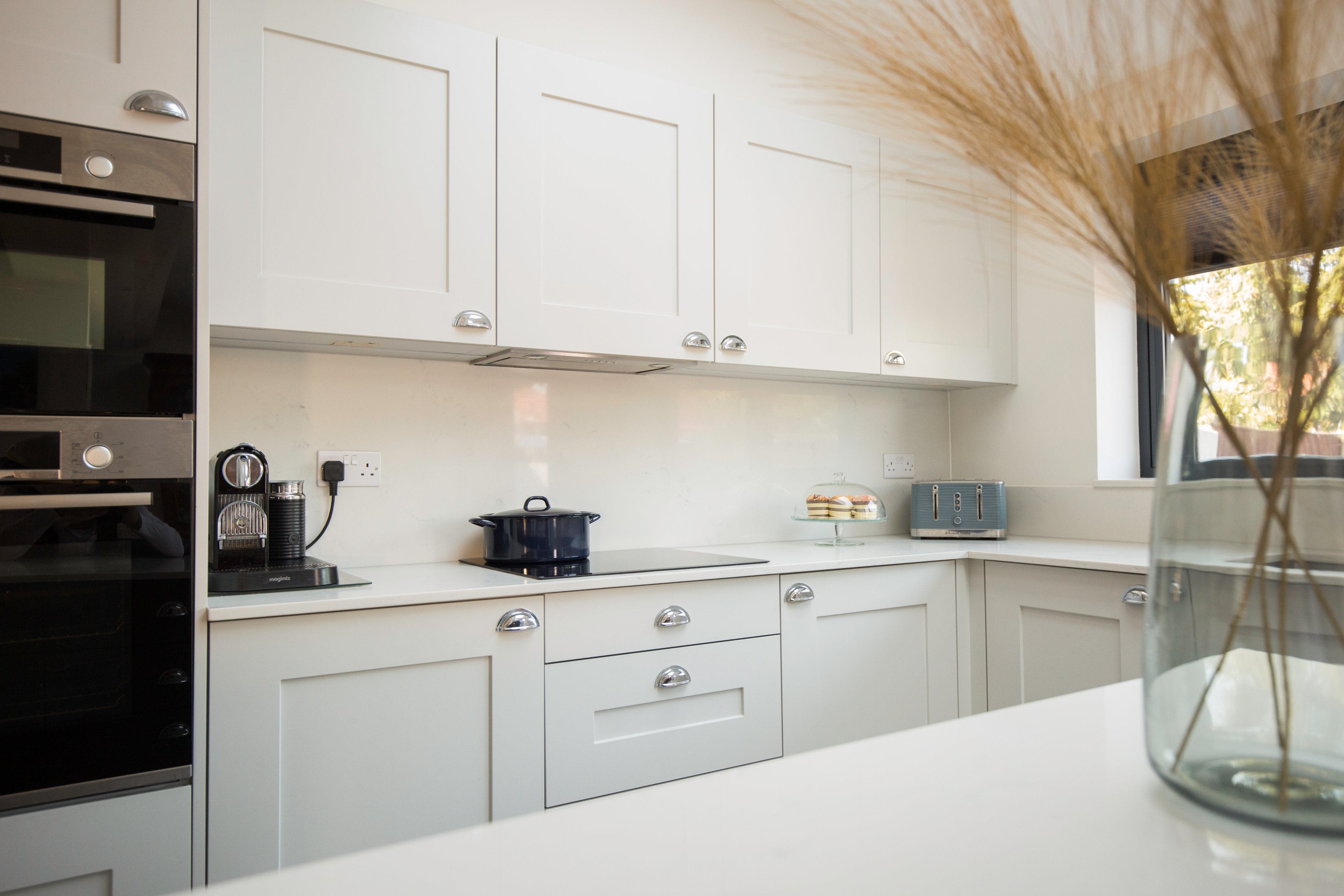 Modern kitchen featuring sleek white cabinetry, a black oven, and a stylish countertop. An Arch KBB team member is present, showcasing the kitchen's sophisticated design elements, including a kettle and a glass vase with decorative foliage. Ideal for home improvement inspiration.