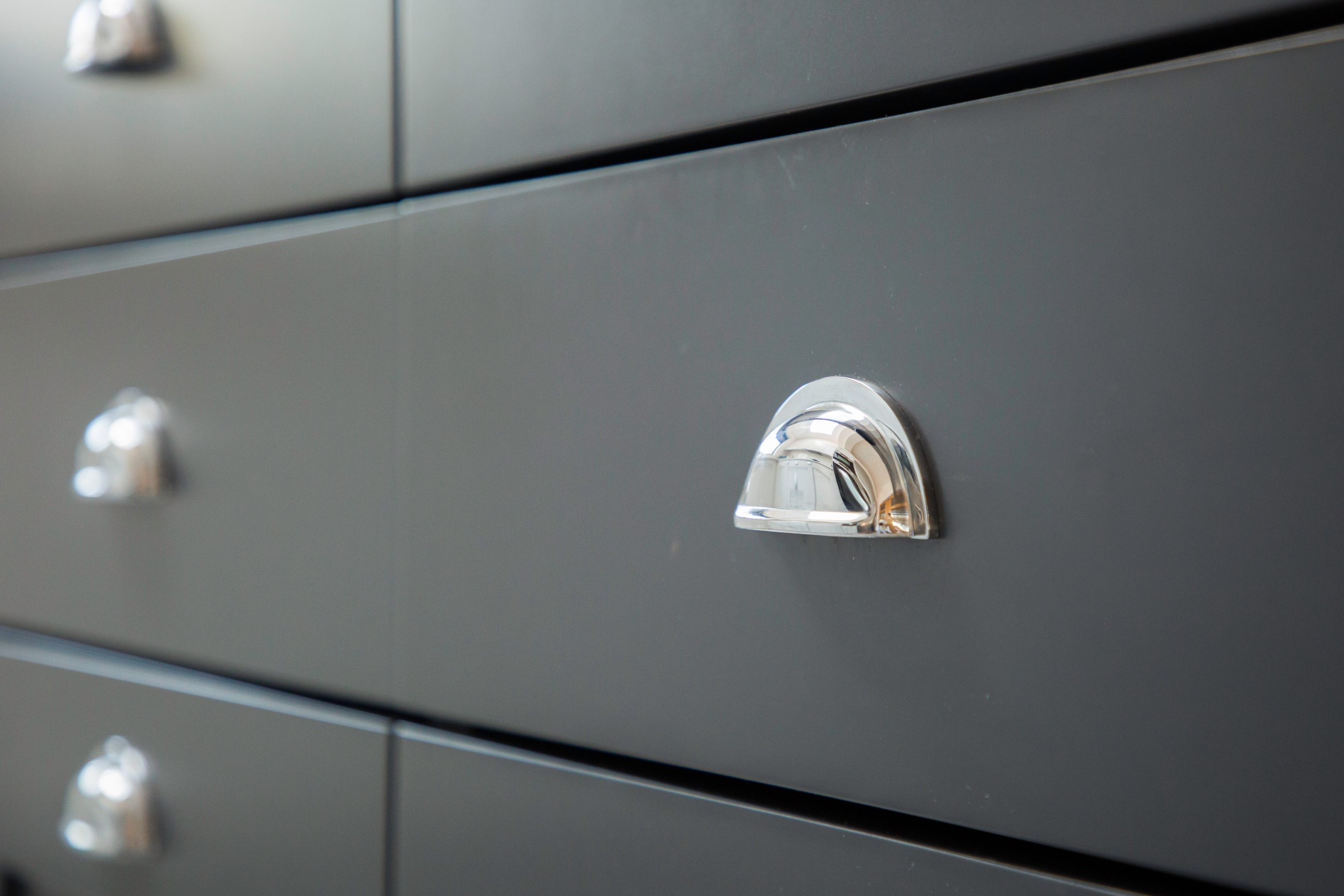 Close-up of a sleek chrome drawer handle on a modern black kitchen cabinet, showcasing contemporary design elements.