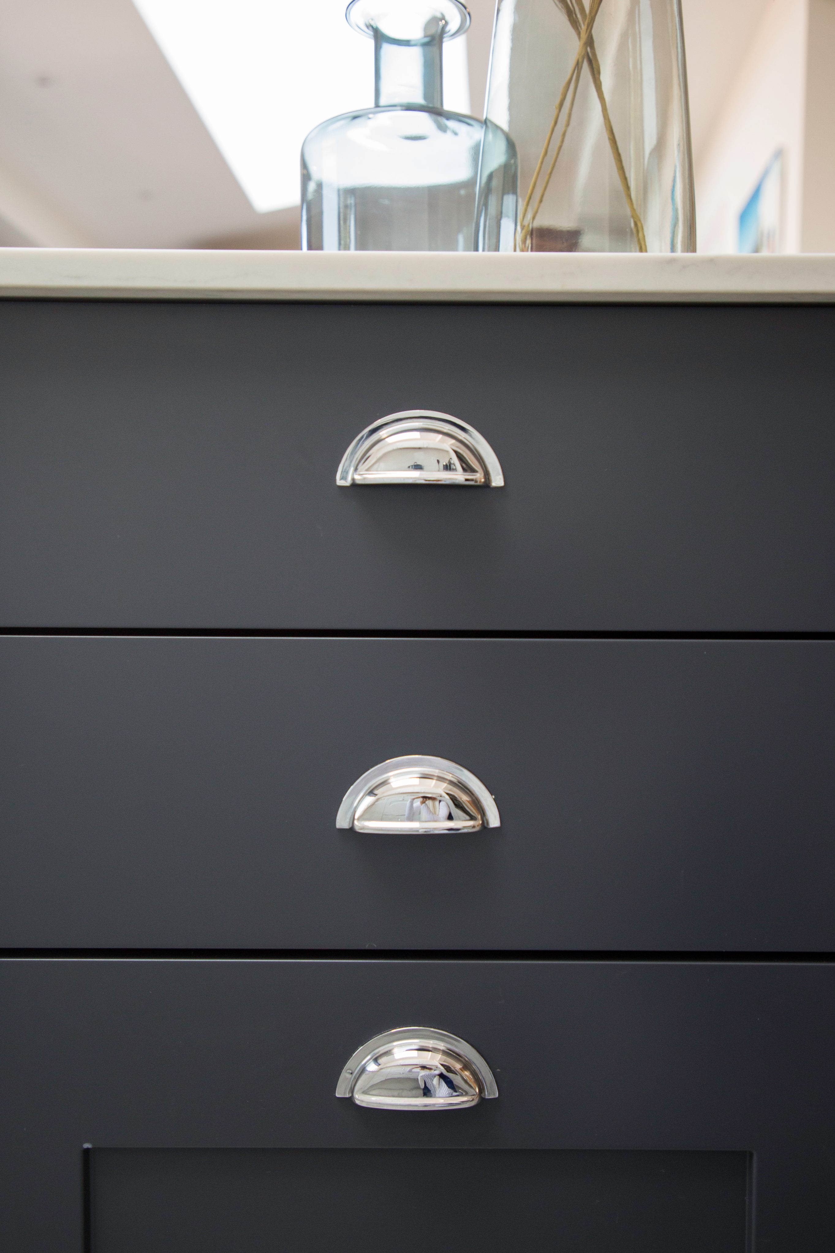 Close-up of two modern drawer handles on a dark cabinet, featuring a sleek chrome finish, showcasing contemporary design elements. An Arch KBB team member is present, providing insights on kitchen and bathroom cabinetry solutions.