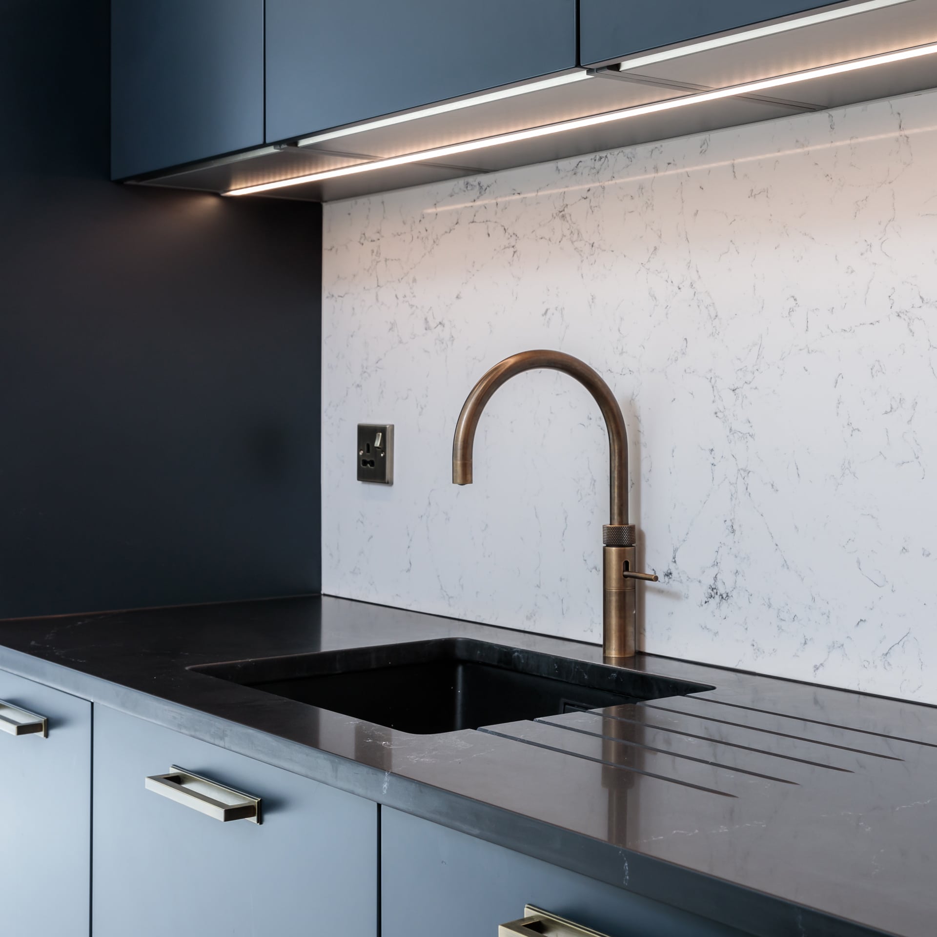 Modern kitchen featuring a sleek black sink and a stylish bronze tap, complemented by a marble-effect splashback and contemporary cabinetry. Ideal for showcasing elegant kitchen design and functionality. Arch KBB team member present.