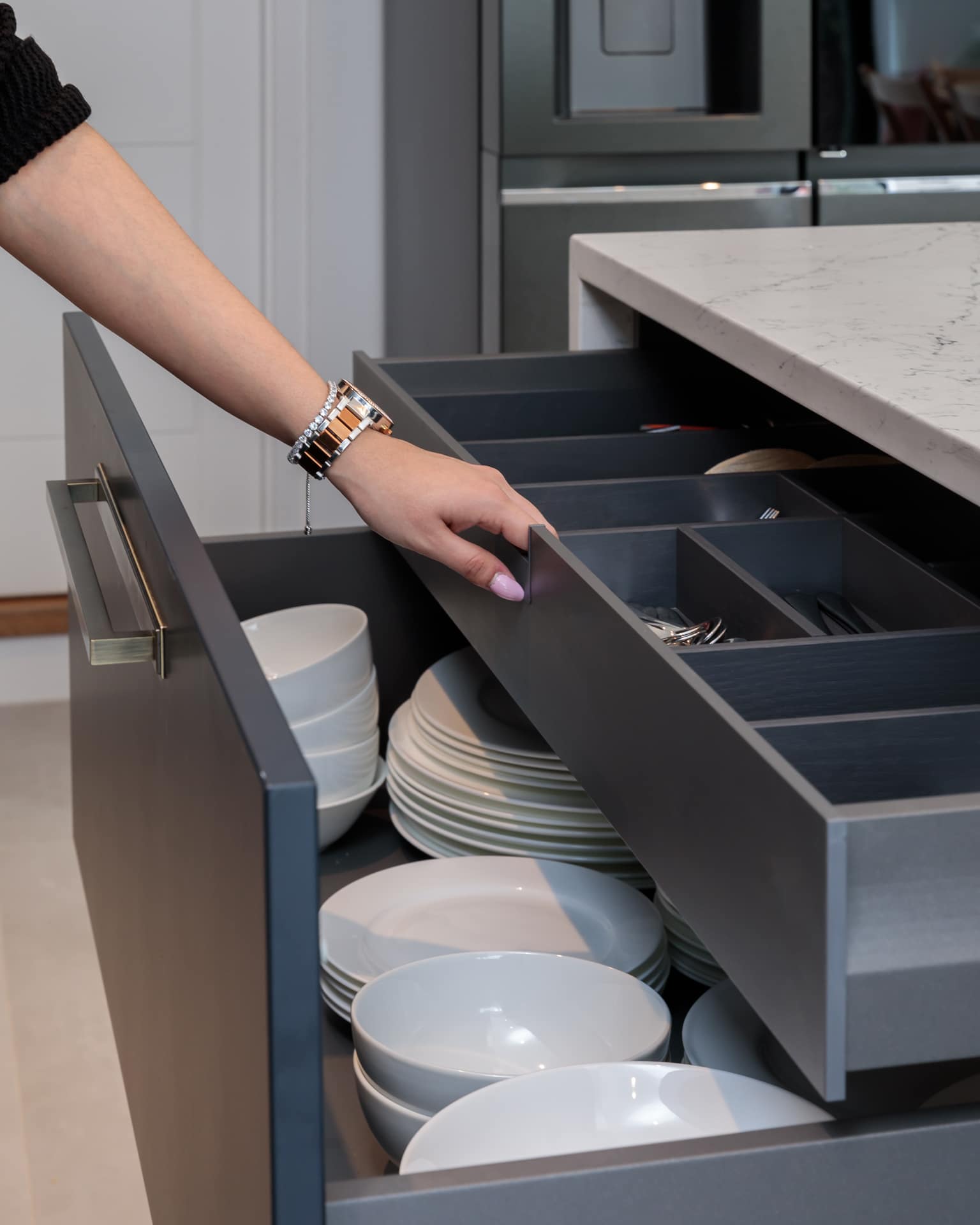 Arch KBB team member organising kitchen utensils in a modern drawer, featuring neatly arranged plates and cutlery, showcasing efficient kitchen storage solutions.