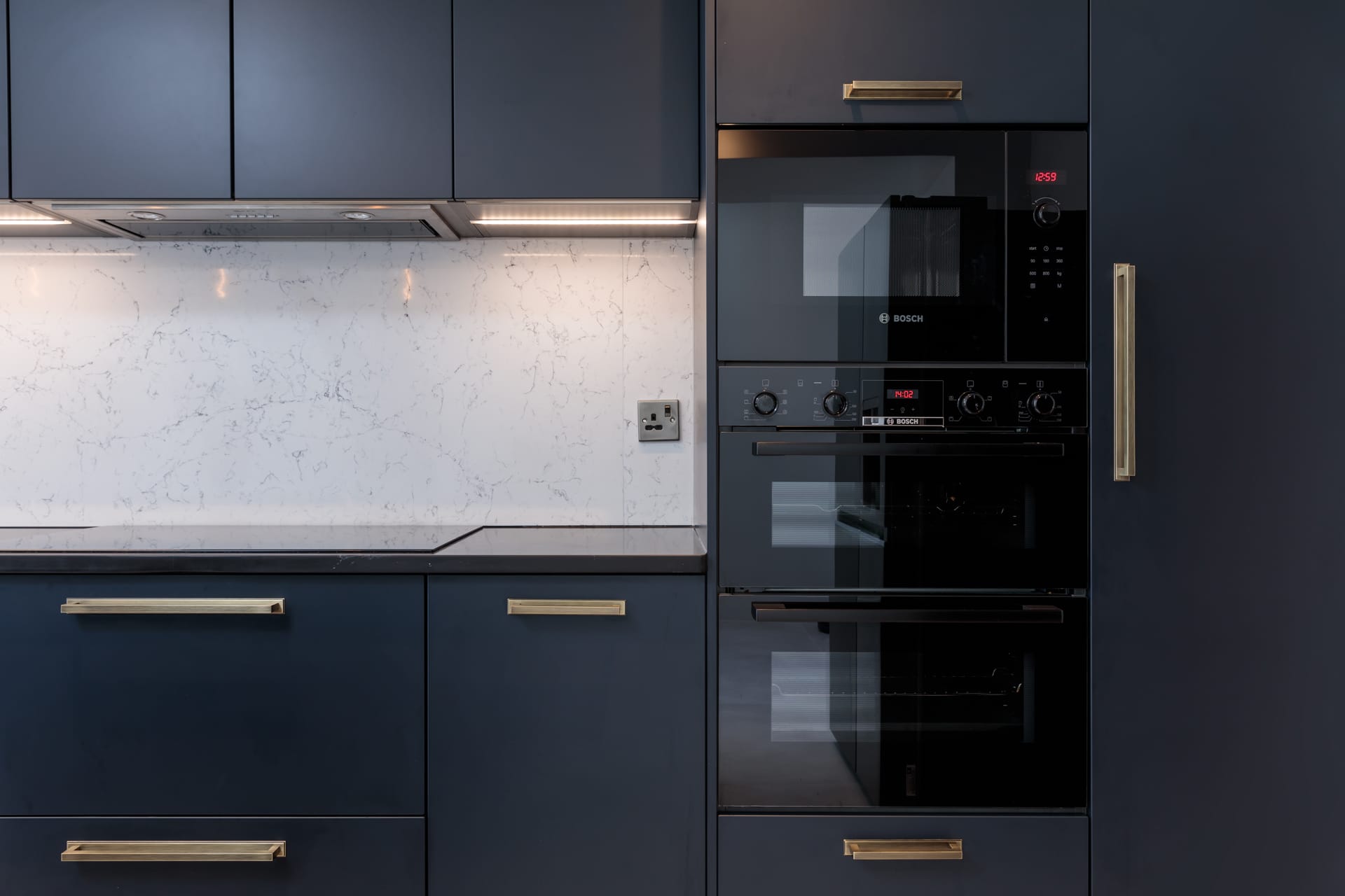 Modern kitchen design featuring sleek dark cabinetry, a stylish marble backsplash, and built-in Bosch appliances. An Arch KBB team member is present, showcasing a contemporary and functional kitchen layout ideal for modern living.