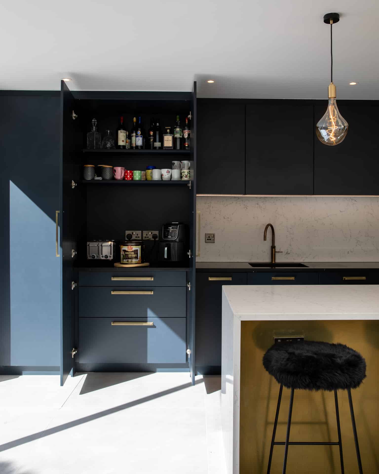 Modern kitchen design featuring dark cabinetry, a stylish countertop, and an array of kitchen appliances. An Arch KBB team member is visible, showcasing the functional layout and contemporary aesthetic of the space. Natural light enhances the details, creating an inviting atmosphere.