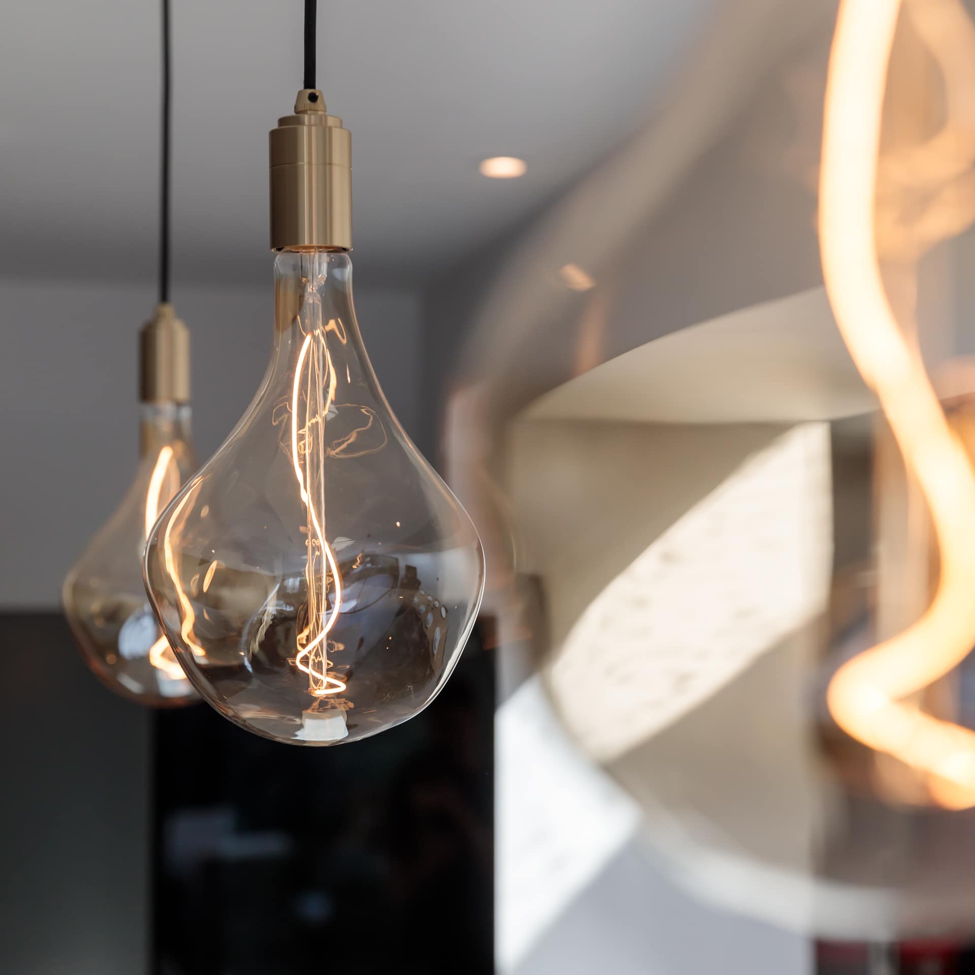 Close-up of stylish glass light bulbs with visible filaments, hanging in a contemporary interior setting, showcasing modern lighting design. An Arch KBB team member is present in the background, contributing to the ambiance of the space.