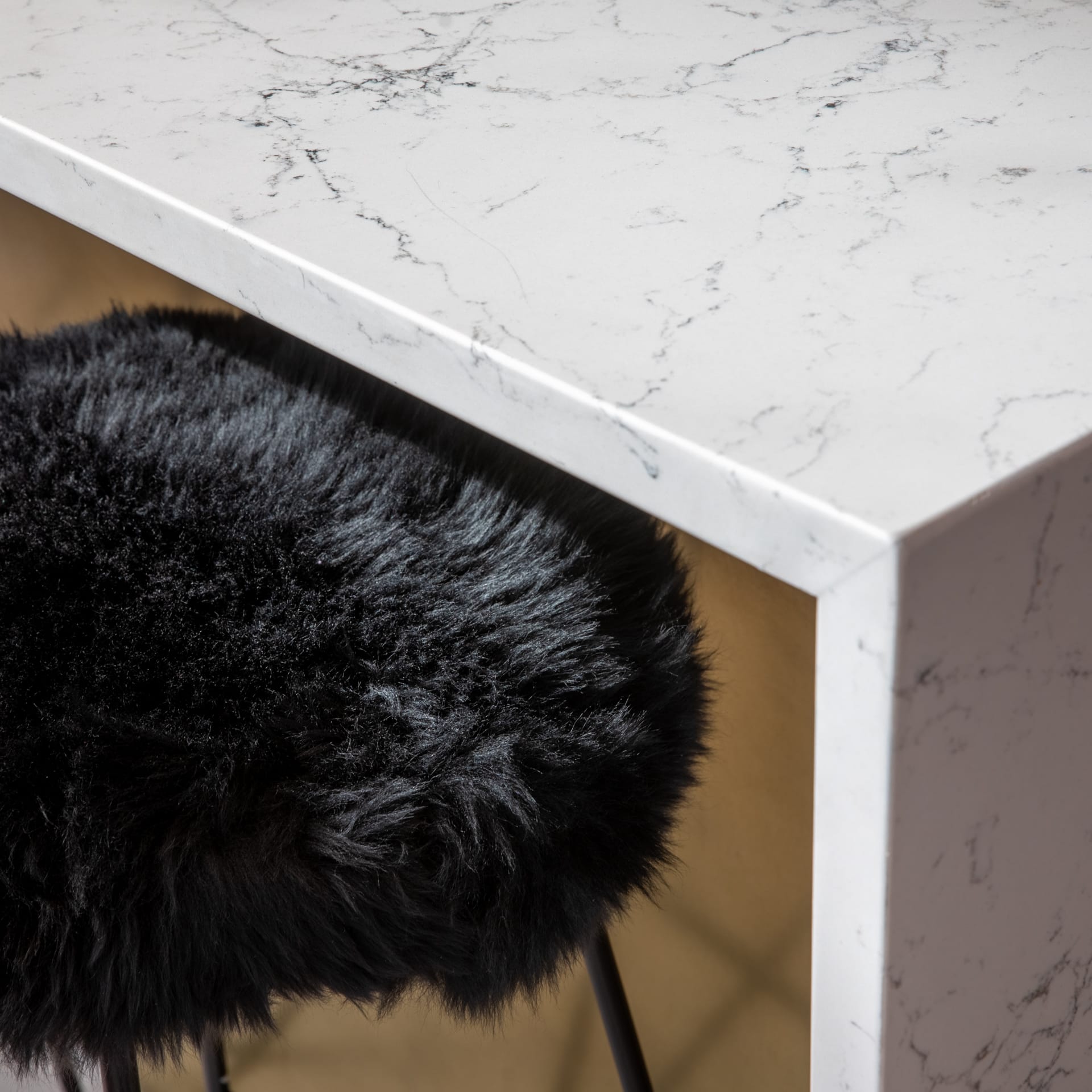 Close-up of a modern tabletop with a marble finish, featuring a plush black stool positioned beneath it. An Arch KBB team member is engaged in a design discussion nearby.