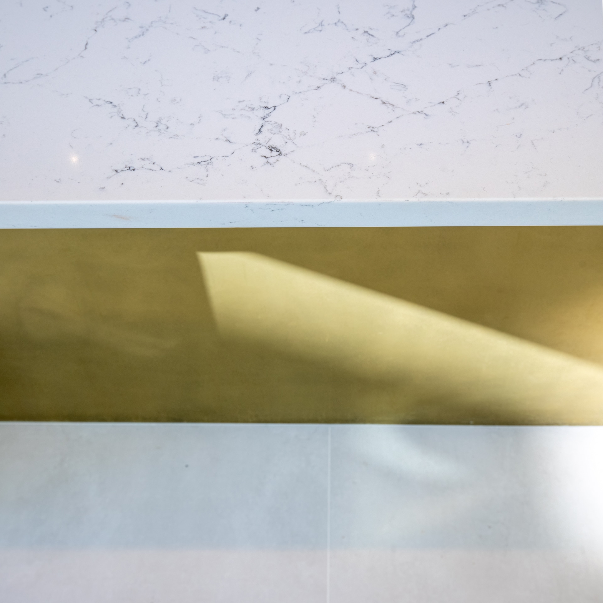 Close-up of a modern surface featuring a polished marble top with grey veining, complemented by a sleek golden strip and a light-coloured base. An Arch KBB team member is present, contributing to the design setup.