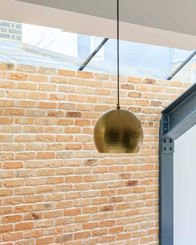 A decorative pendant light hangs from the ceiling, casting a warm glow against a backdrop of exposed brick walls in a modern interior space, showcasing a blend of contemporary design and rustic charm. An Arch KBB team member is present, adding to the atmosphere of the setting.