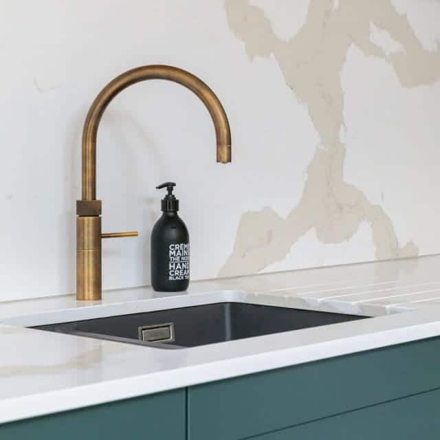 Modern kitchen sink featuring a stylish brass tap and a black hand cream dispenser on a marble countertop, with a minimalist design and neutral wall backdrop. Ideal for contemporary interior design inspiration.