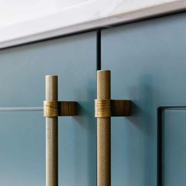 Close-up of stylish cabinet handles on a blue kitchen cabinet, featuring textured gold accents, designed for modern interior aesthetics. Arch KBB team member present for scale.