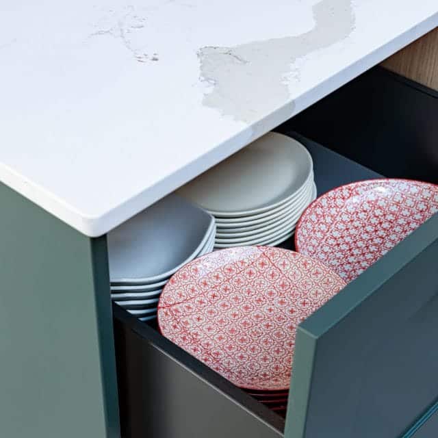 A neatly organised kitchen drawer containing a stack of plain white plates and decorative red patterned plates, showcasing efficient storage solutions for kitchenware. An Arch KBB team member is involved in the arrangement.