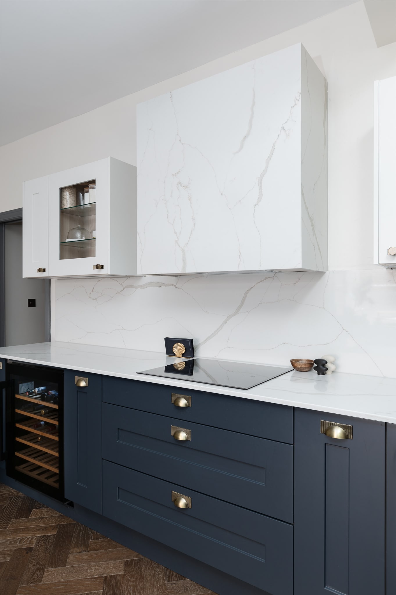 Modern kitchen design featuring a sleek white marble backsplash, navy blue cabinetry with brass handles, and a built-in wine cooler. An Arch KBB team member is present, showcasing contemporary kitchen aesthetics and functionality.