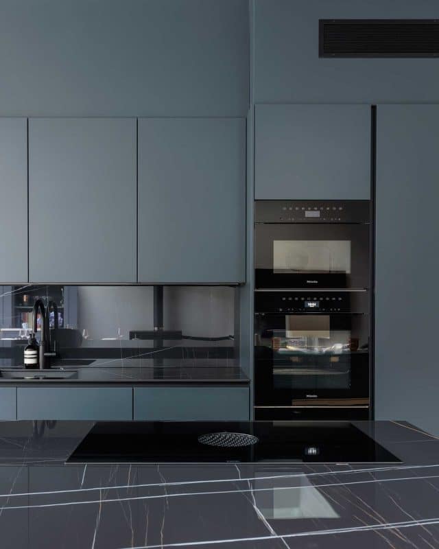 Modern kitchen featuring sleek blue cabinetry, a black countertop, and built-in black appliances, including ovens. An Arch KBB team member is present, enhancing the design experience.