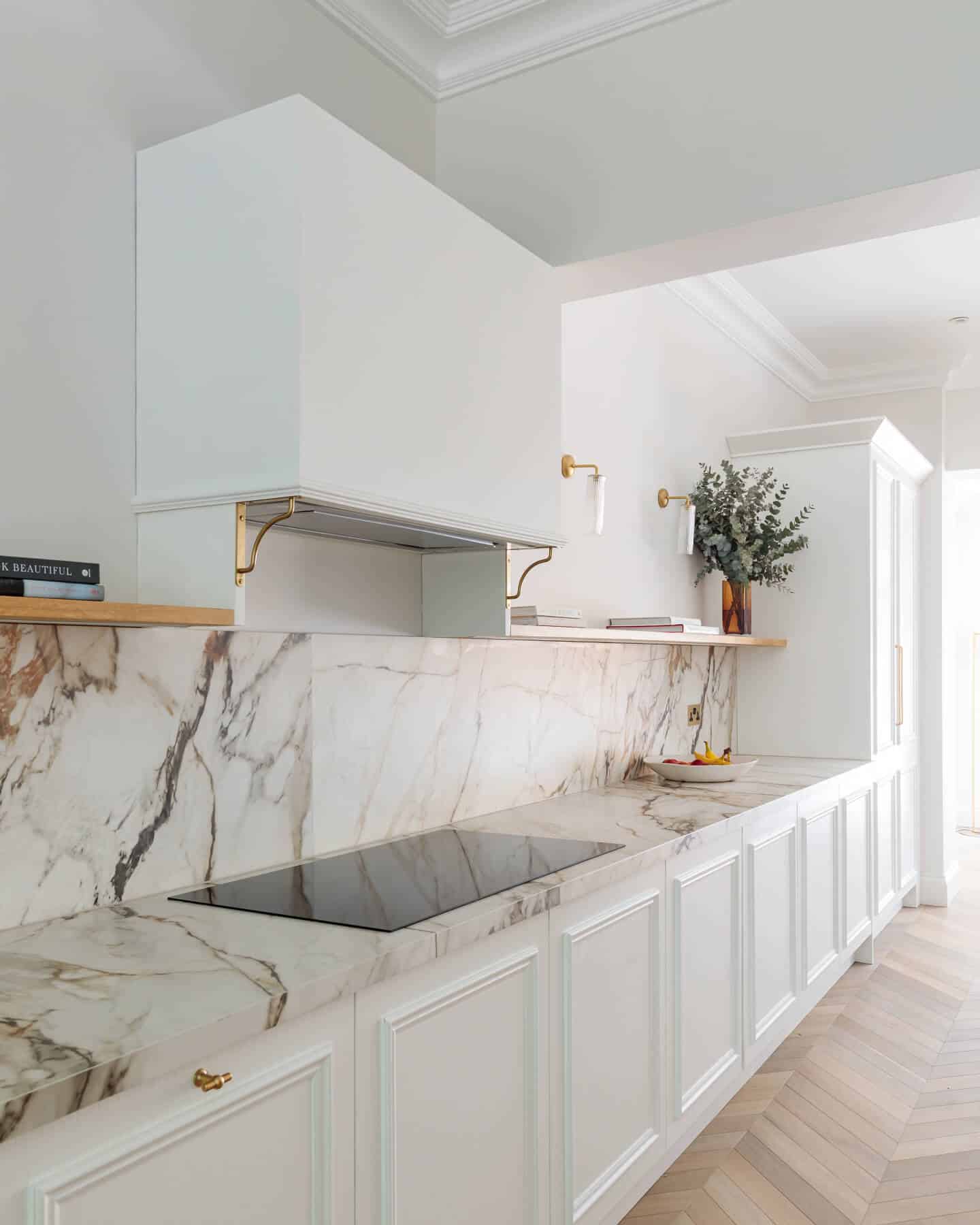 Modern kitchen design featuring a sleek marble splashback and a minimalist aesthetic. The space includes an integrated cooktop, stylish cabinetry, and decorative elements such as a vase with greenery. An Arch KBB team member is present, contributing to the kitchen's elegant atmosphere.