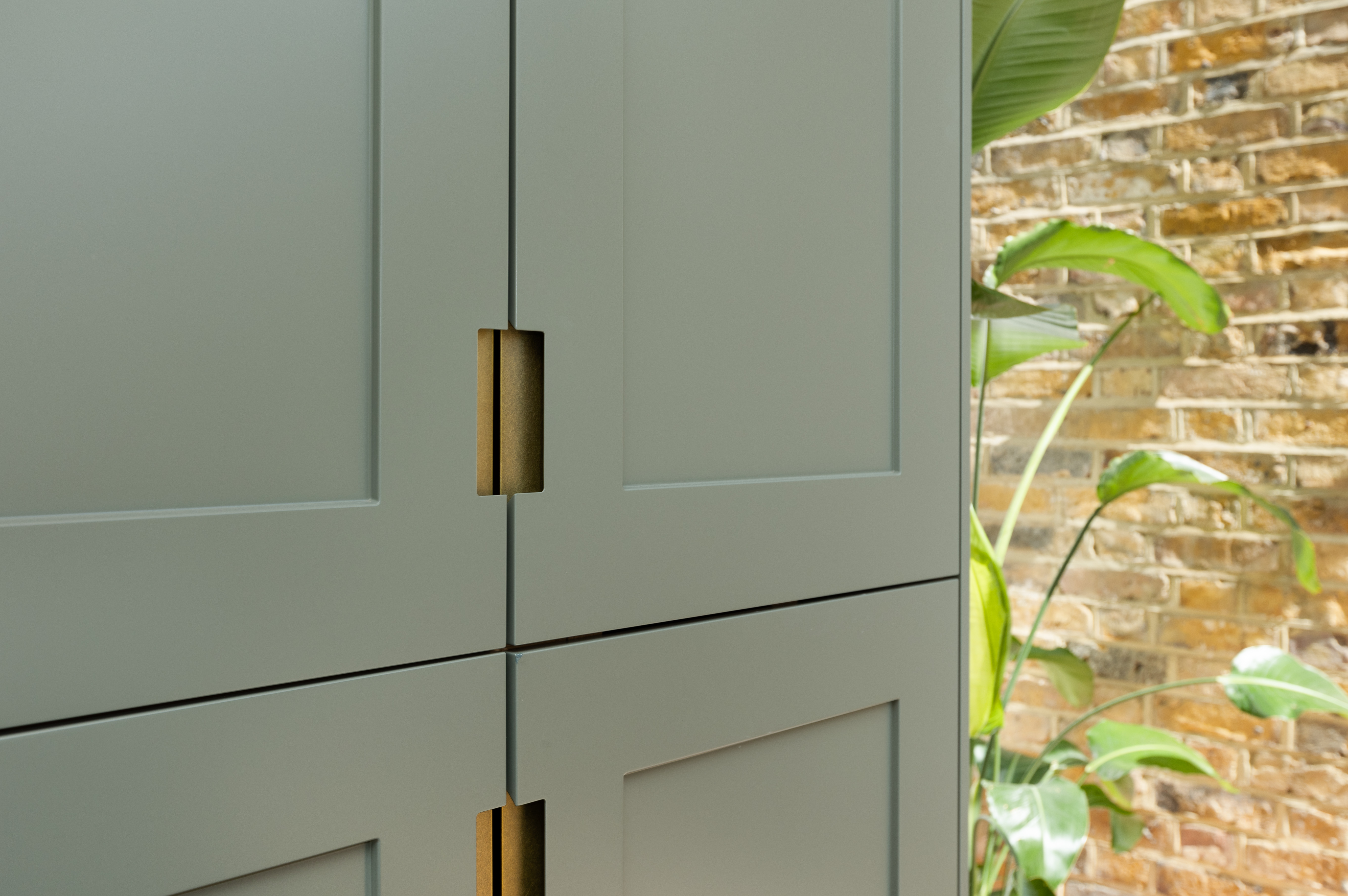 Close-up of a stylish grey cabinetry design featuring unique cut-out handles, complemented by lush greenery in the background, showcasing modern interior aesthetics. An Arch KBB team member is present, adding to the design consultation atmosphere.