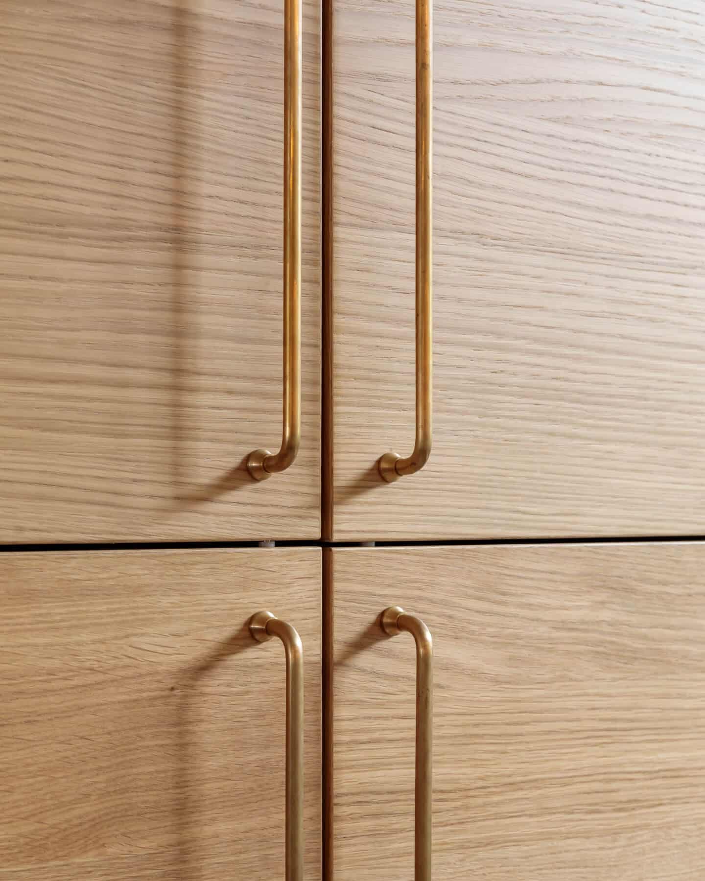 Close-up of wooden cabinet doors featuring sleek gold handles, showcasing modern design elements and craftsmanship by an Arch KBB team member.