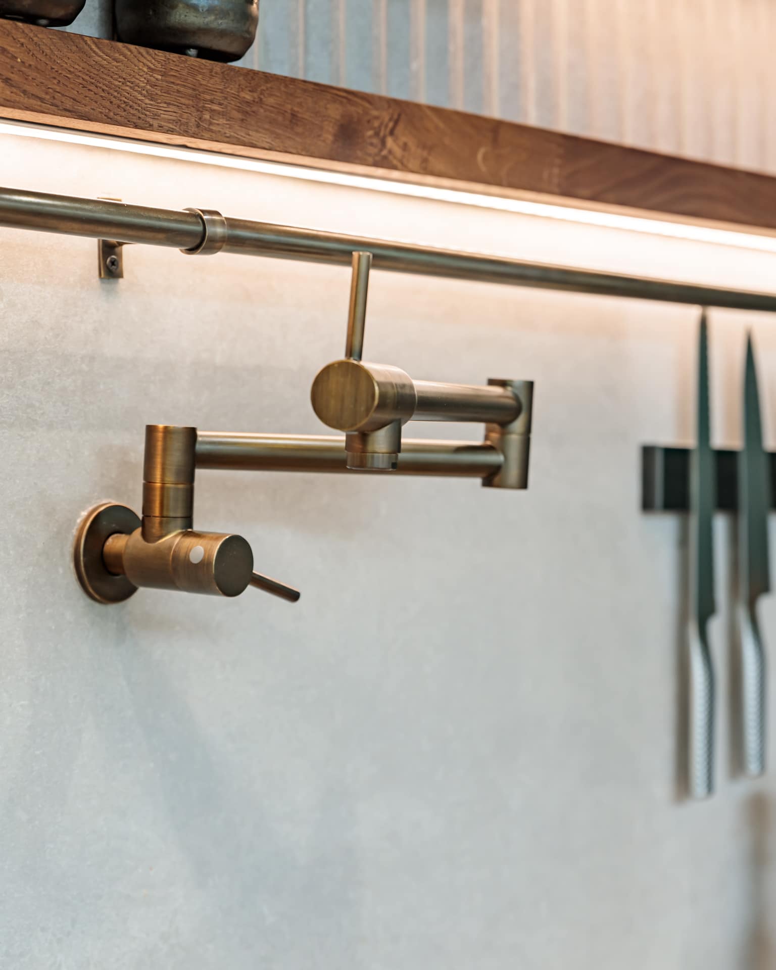Close-up of a stylish brass kitchen tap mounted on a wall, featuring a sleek design and modern functionality, with a backdrop of kitchen knives for added context. An Arch KBB team member is present, contributing to the kitchen's aesthetic.