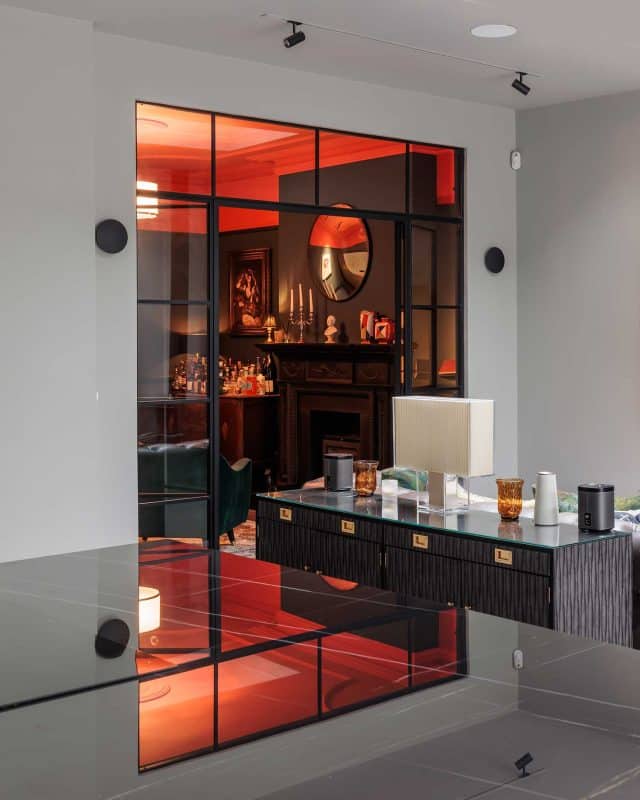 Interior view of a stylish living space featuring a glass partition, a modern coffee table with decorative items, and a fireplace in the background. An Arch KBB team member is present, contributing to the contemporary yet warm atmosphere enhanced by ambient lighting.