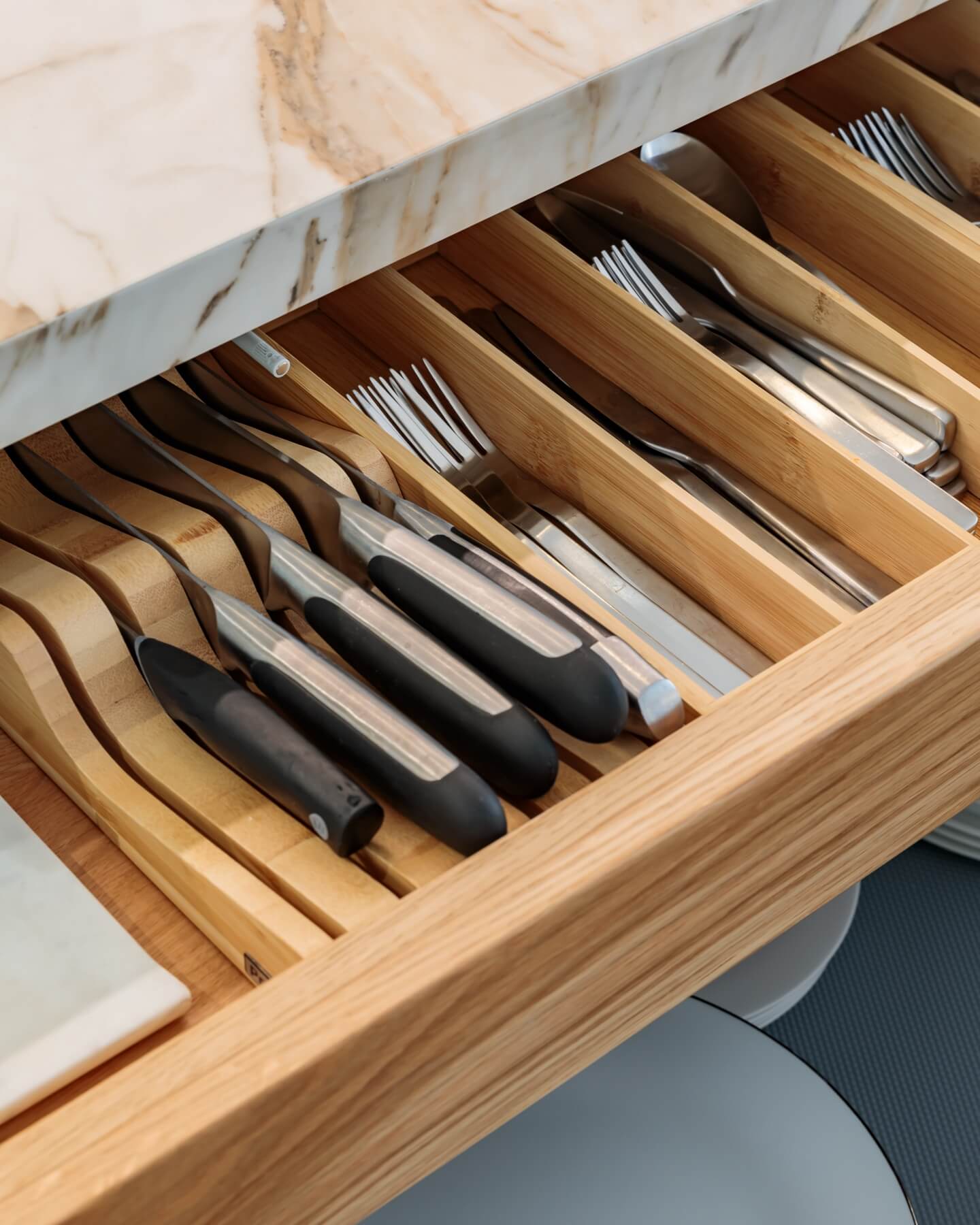 A neatly organized kitchen drawer featuring various utensils, including knives, forks, and tongs, arranged in bamboo dividers. An Arch KBB team member is present, ensuring the kitchen's functionality and aesthetic appeal.