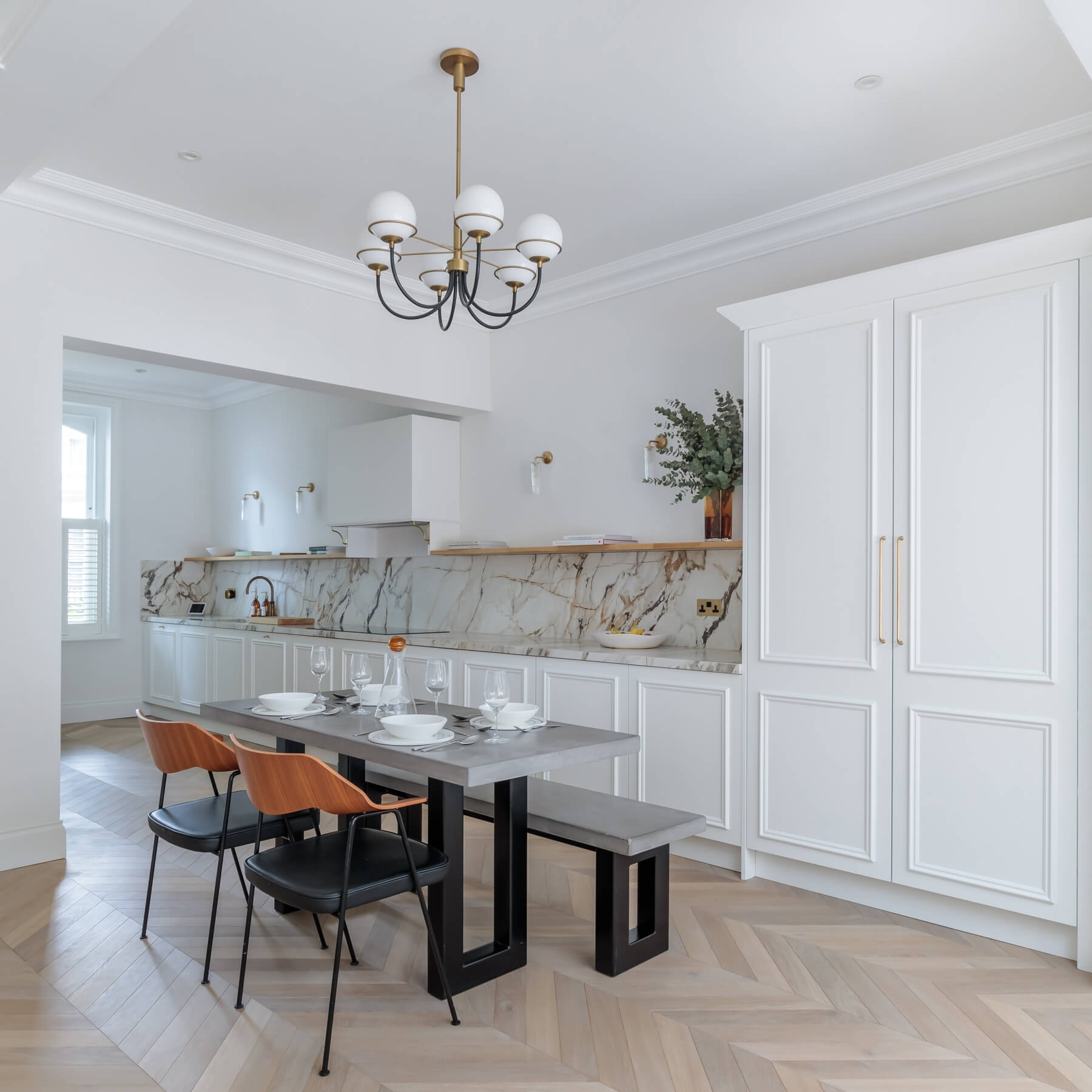 Modern kitchen and dining area featuring a sleek marble backsplash, white cabinetry, and stylish wooden and black seating. The space is illuminated by a contemporary chandelier, creating an inviting atmosphere for dining and entertaining. An Arch KBB team member is present, showcasing the design's functionality and aesthetic appeal.