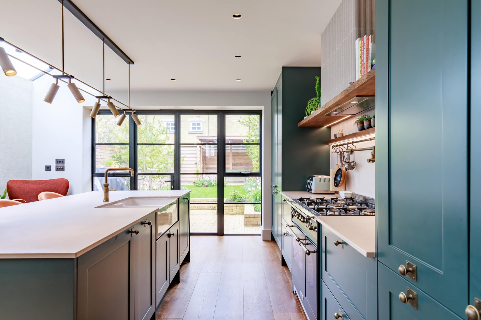 Modern kitchen featuring a spacious layout with a central island, stylish cabinetry in green tones, and stainless steel appliances. Natural light floods the space through large windows, highlighting the contemporary design and inviting atmosphere. An Arch KBB team member is present, showcasing the kitchen's functionality and aesthetic appeal.