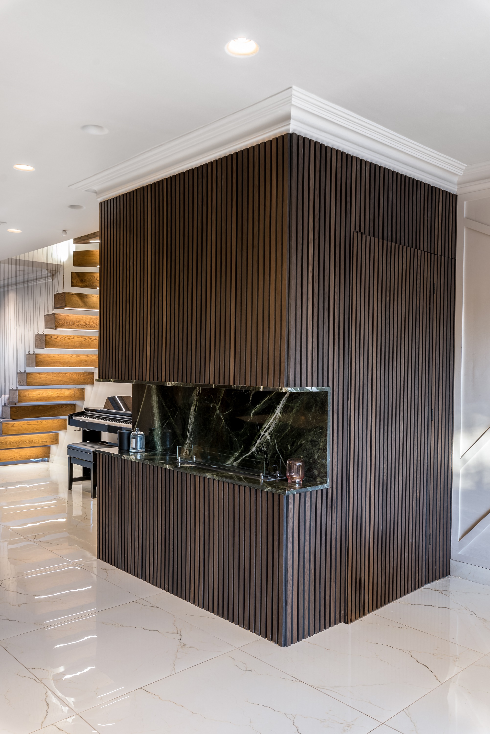 Interior view of a modern kitchen featuring a wooden slatted wall, a marble countertop, and a staircase in the background. An Arch KBB team member is present, adding to the design atmosphere. The stylish space highlights contemporary design elements and finishes.
