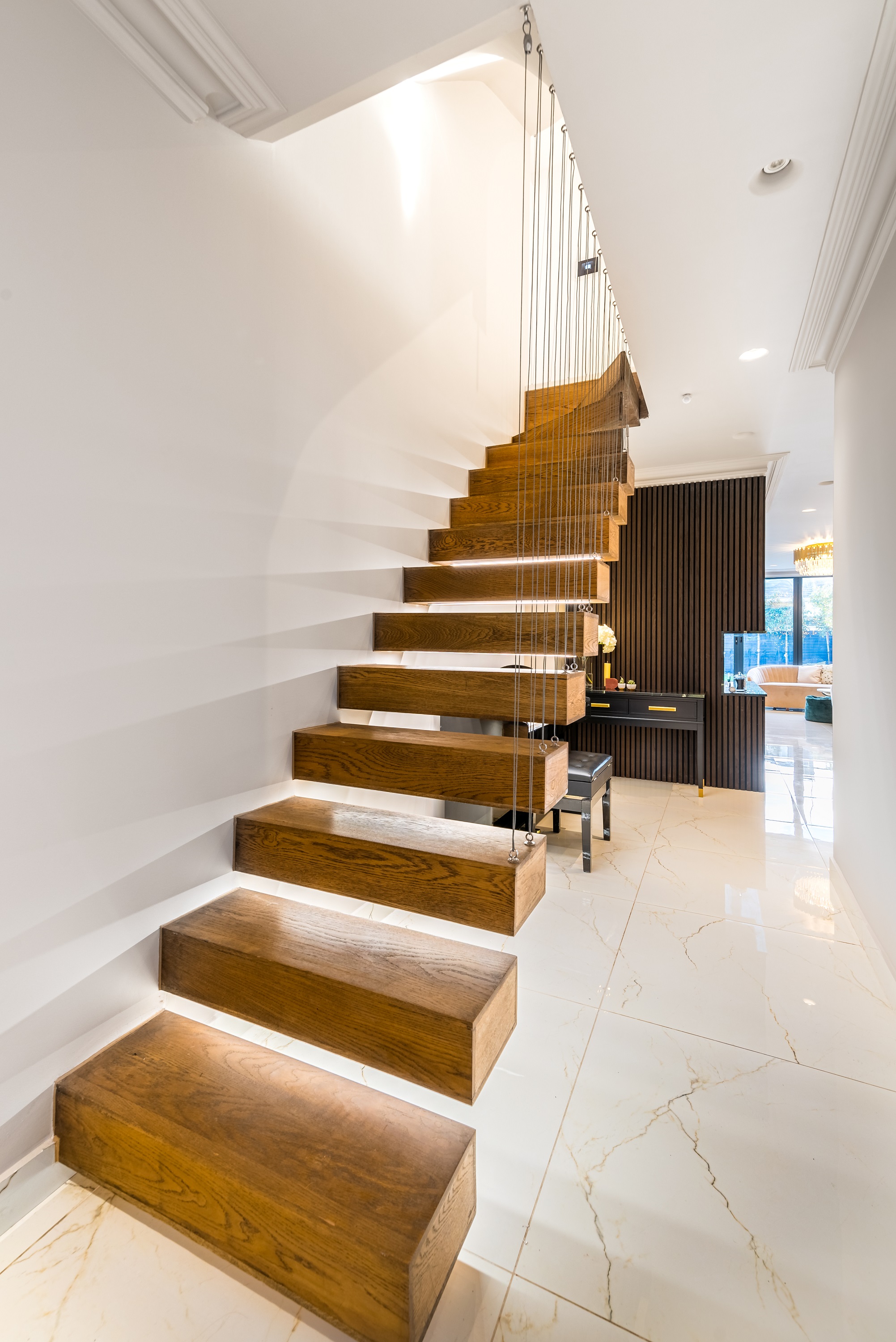 Modern wooden staircase with illuminated steps, leading to a bright interior space. An Arch KBB team member is visible in the background, enhancing the contemporary design of the home. The setting features elegant furnishings and a stylish decor.