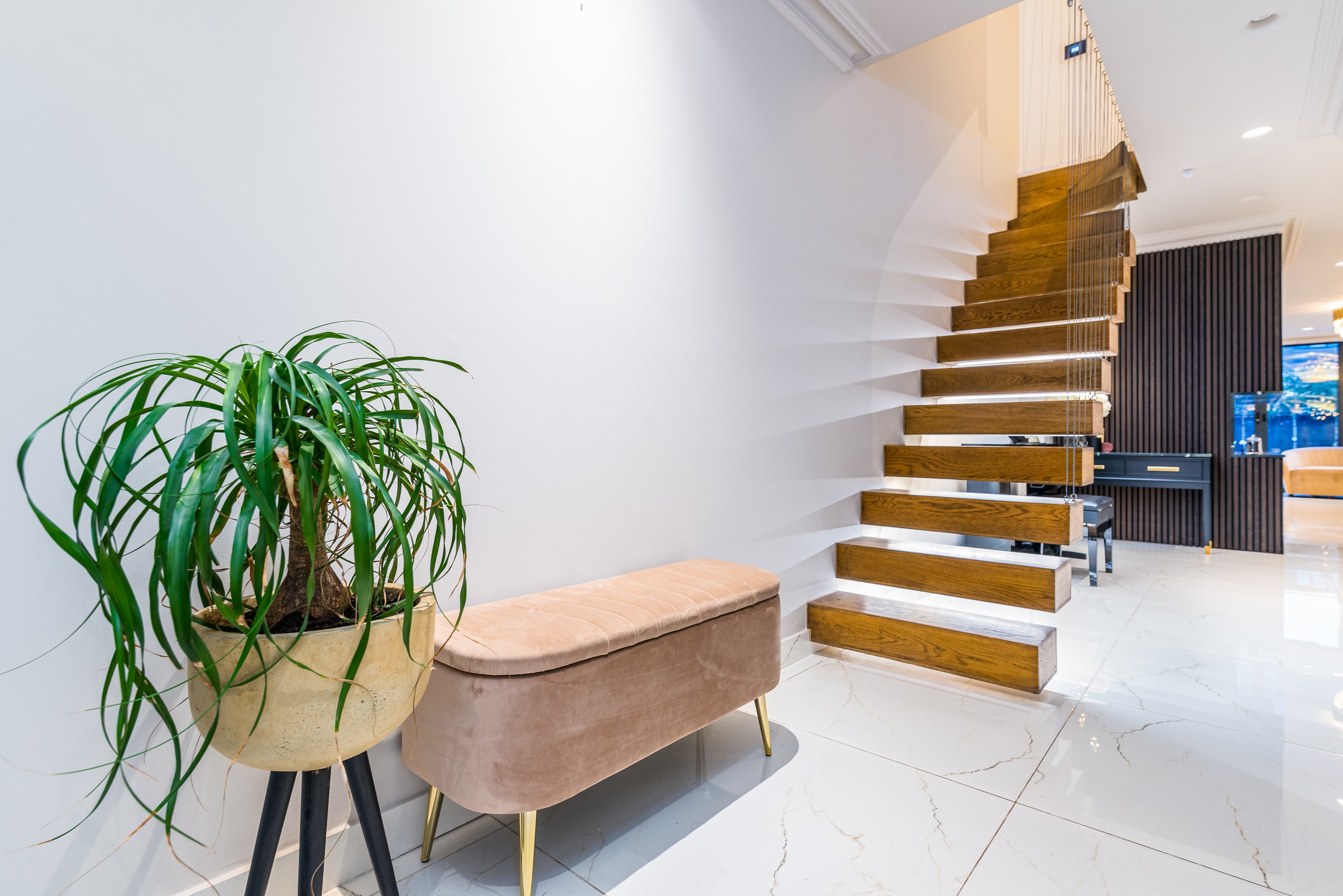 Modern interior staircase with wooden steps, a stylish bench, and a decorative potted plant in a bright hallway, featuring sleek tiles and minimalist design elements, showcasing the work of an Arch KBB team member.
