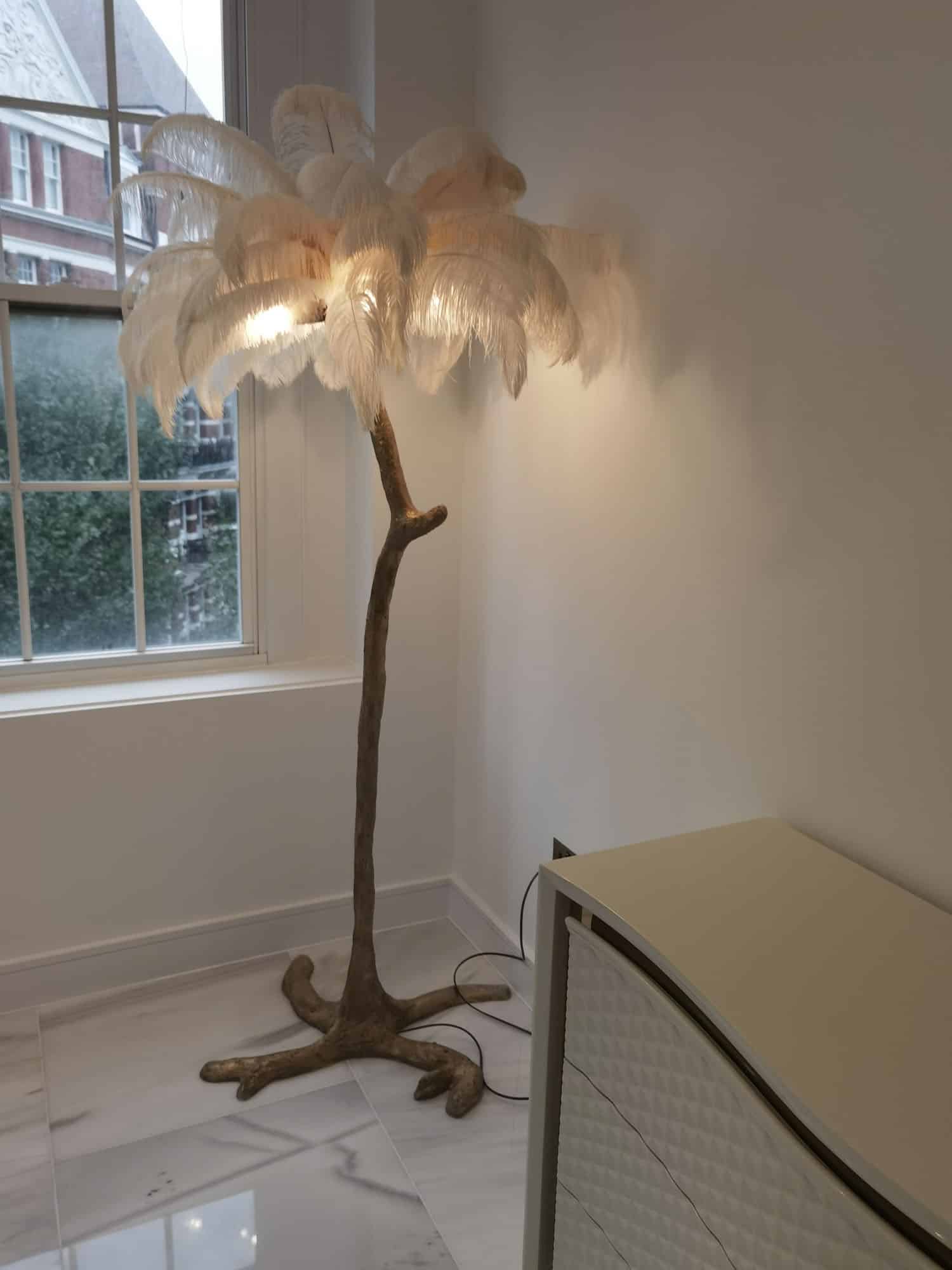 A stylish feather lamp with a natural wood base, illuminating a bright interior space next to a window, enhancing the room's aesthetic appeal. An Arch KBB team member is present in the scene.
