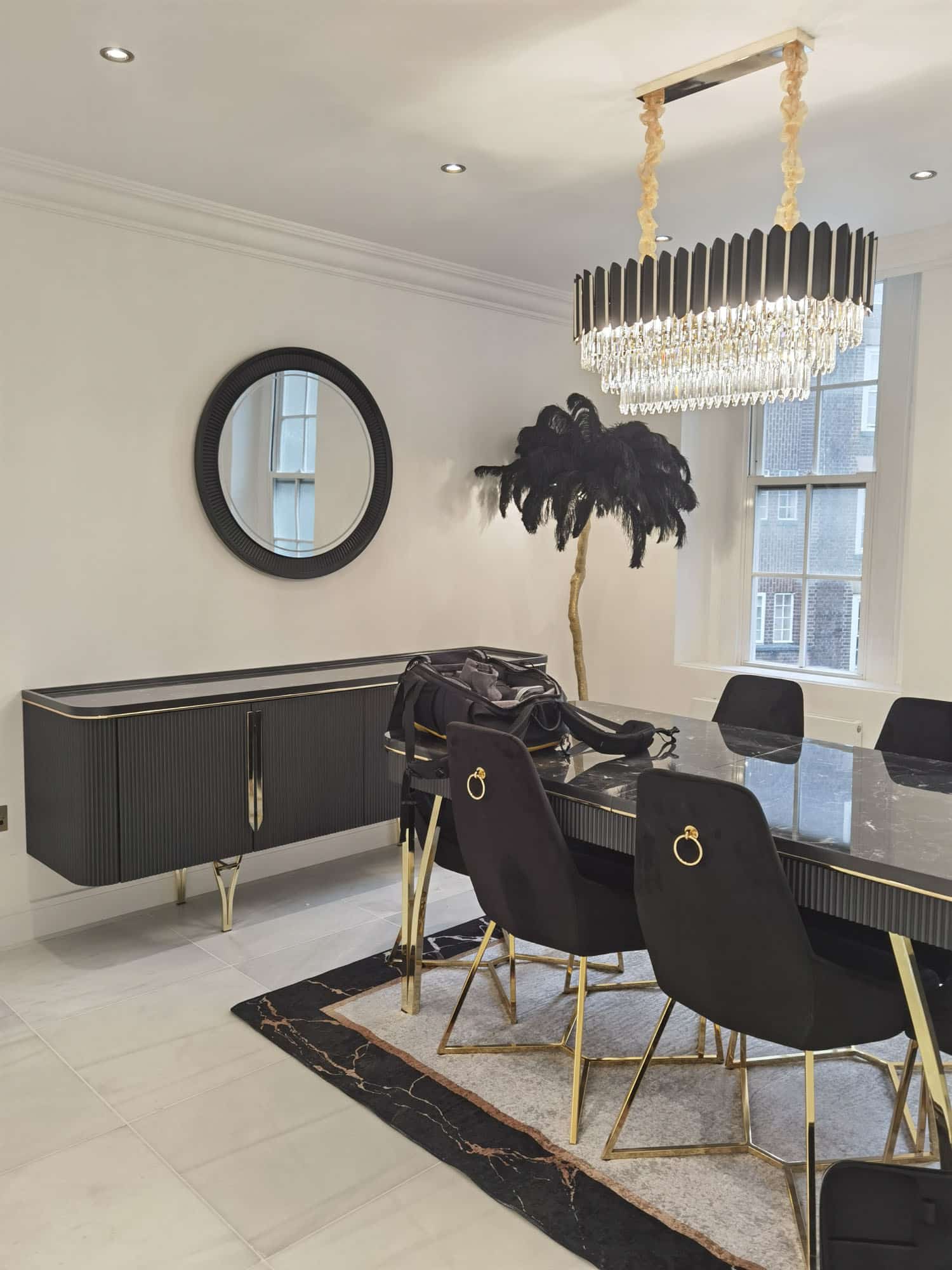 Modern dining area featuring a sleek black sideboard, a large round mirror, and a statement chandelier. An elegant dining table surrounded by stylish black chairs complements the sophisticated decor, while a decorative plant adds a touch of greenery. An Arch KBB team member is present, contributing to the scene.