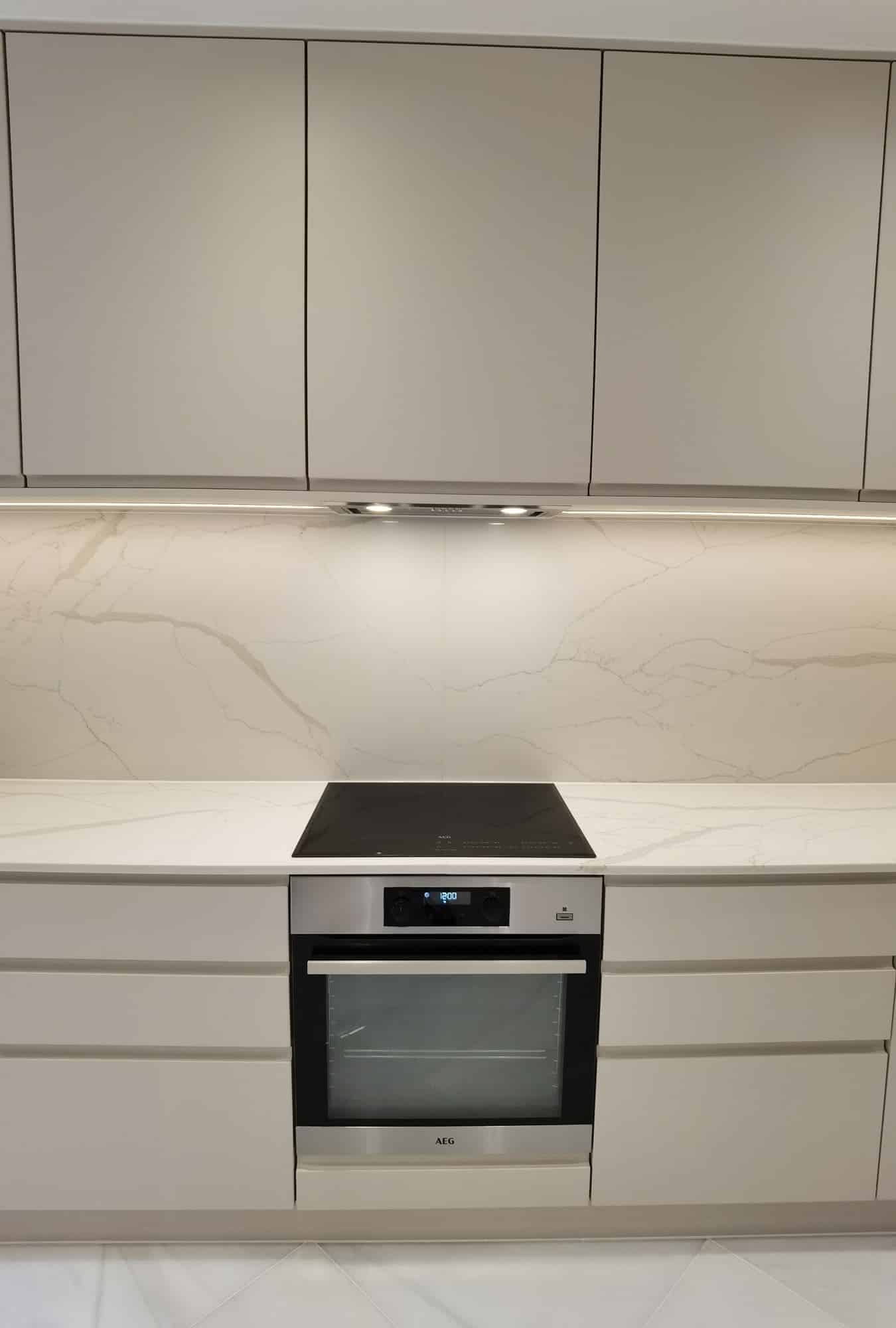 Modern kitchen interior featuring a sleek induction cooktop, built-in oven, and elegant marble splashback. The design showcases minimalist cabinetry and integrated lighting, creating a contemporary and inviting atmosphere. An Arch KBB team member is present, contributing to the kitchen's stylish aesthetic.