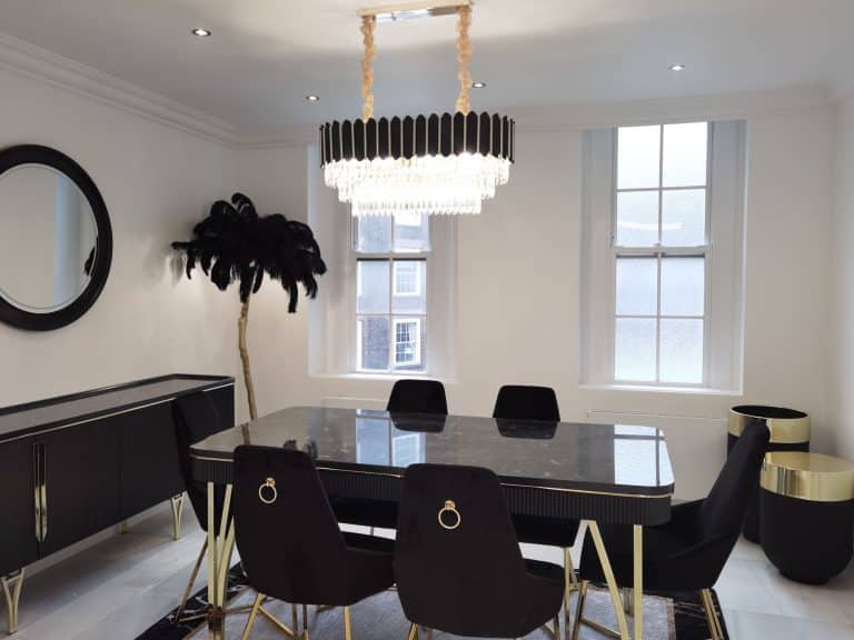 Modern dining area featuring a sleek black table surrounded by stylish chairs, complemented by a striking chandelier and a decorative plant. An Arch KBB team member is present, enhancing the contemporary design aesthetic.