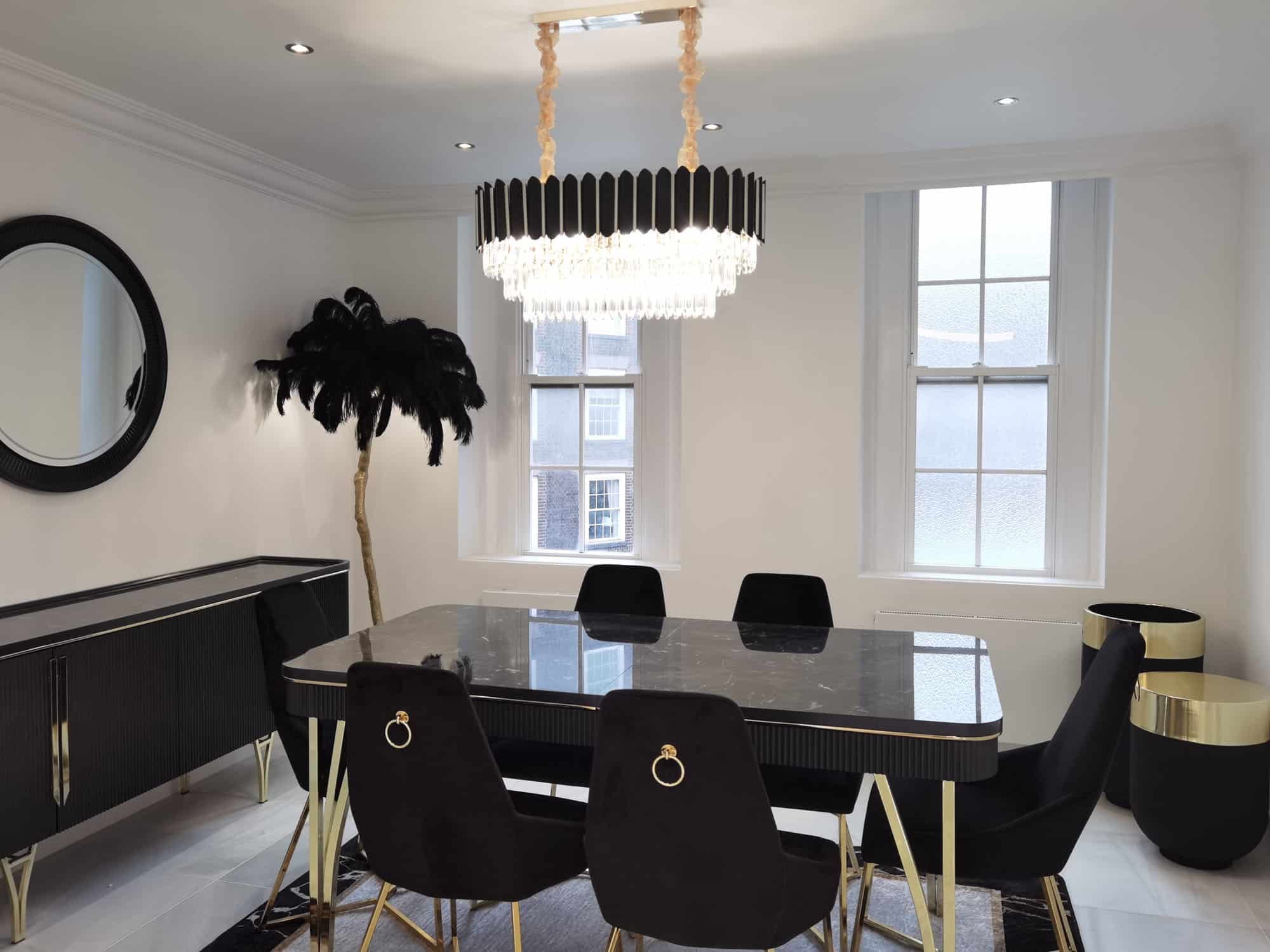 Modern dining area featuring a sleek black table surrounded by stylish chairs, complemented by a striking chandelier and a decorative plant. An Arch KBB team member is present, enhancing the contemporary design aesthetic.
