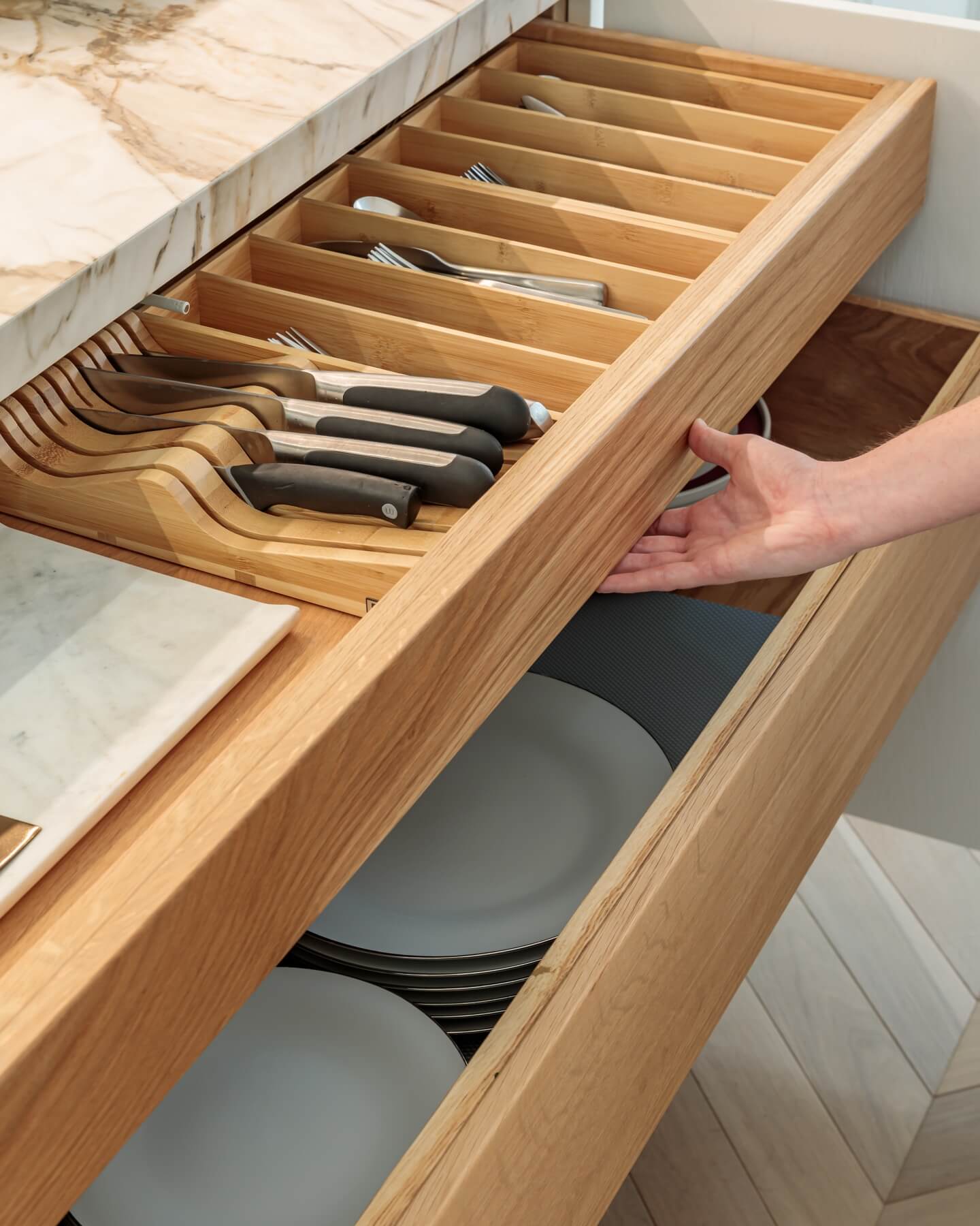 Arch KBB team member demonstrating an organised kitchen drawer featuring cutlery and plates, showcasing modern storage solutions in a stylish kitchen design.