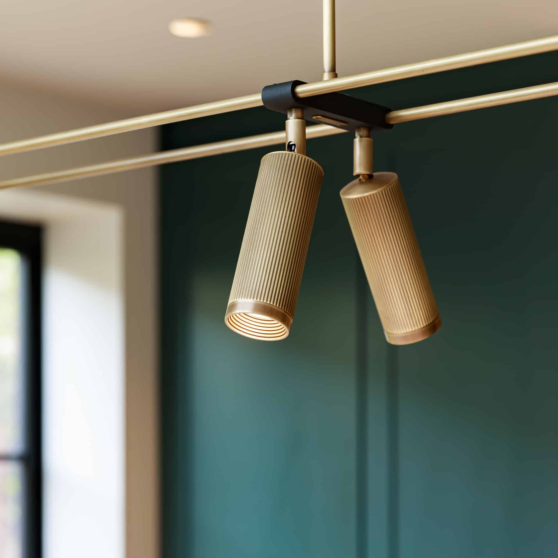 Modern pendant lighting with ribbed design, suspended from a sleek track against a deep green wall, enhancing interior decor. An Arch KBB team member is present, contributing to the design ambiance.