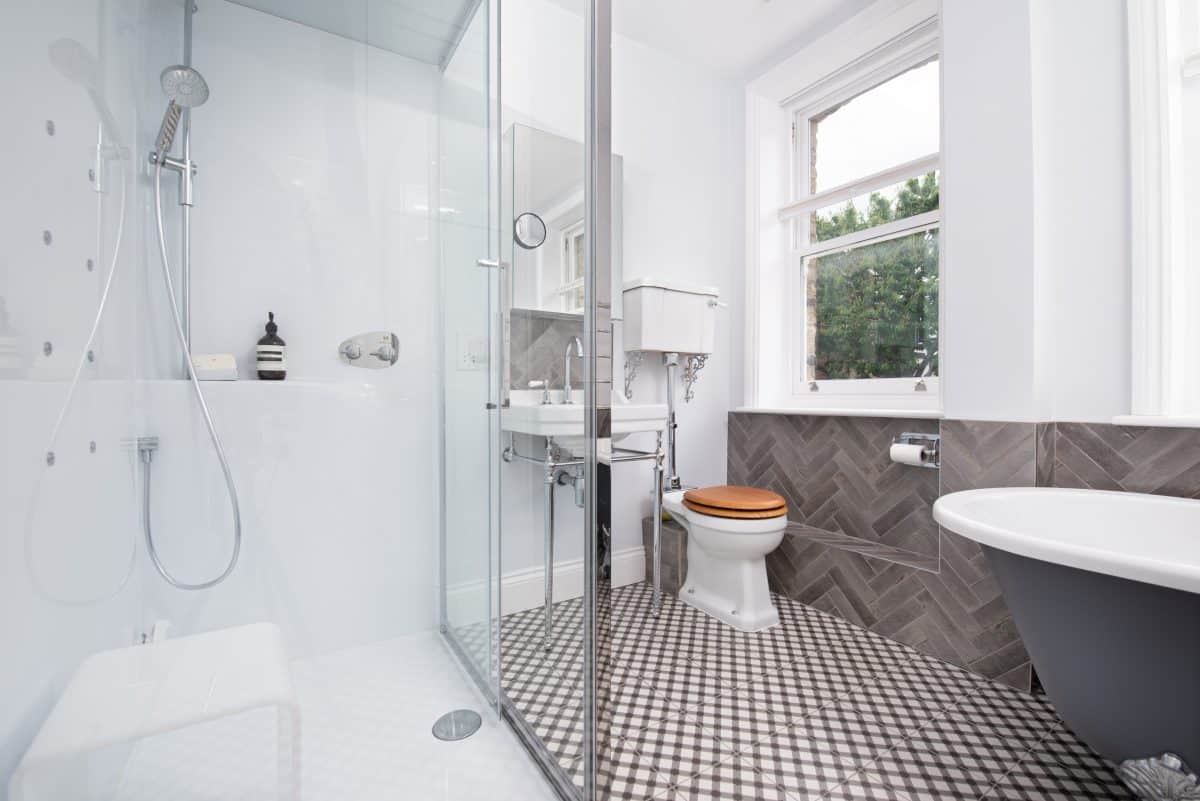 Modern bathroom featuring a walk-in shower, sleek basin, and stylish toilet. The floor is adorned with a patterned tile design, while large windows provide natural light and a view of greenery outside. An Arch KBB team member is present, enhancing the design consultation experience.