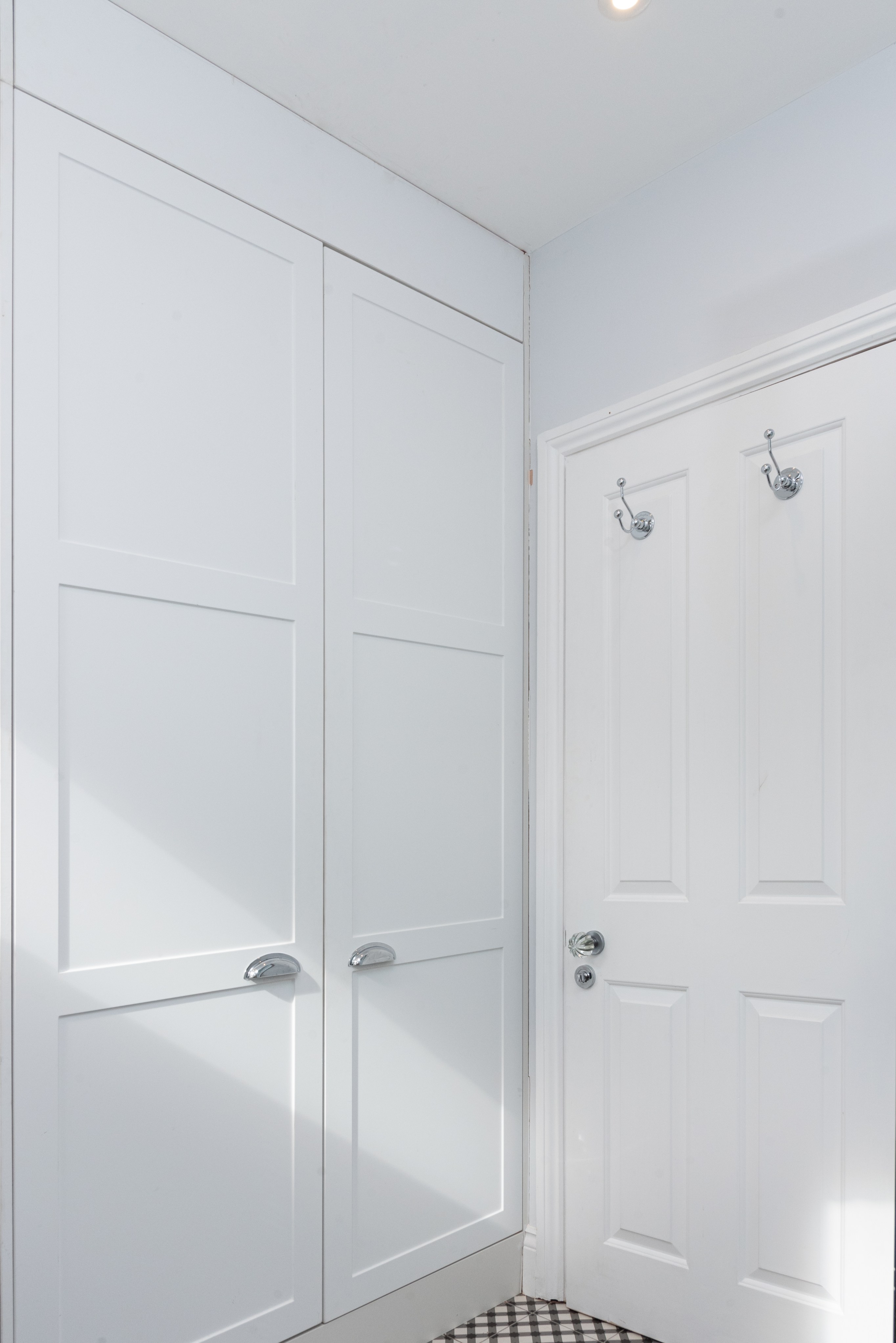 Interior view of a modern hallway featuring white cabinetry and a door. The bright space is enhanced by natural light, highlighting the clean lines and minimalist design. An Arch KBB team member is present, contributing to the stylish environment.