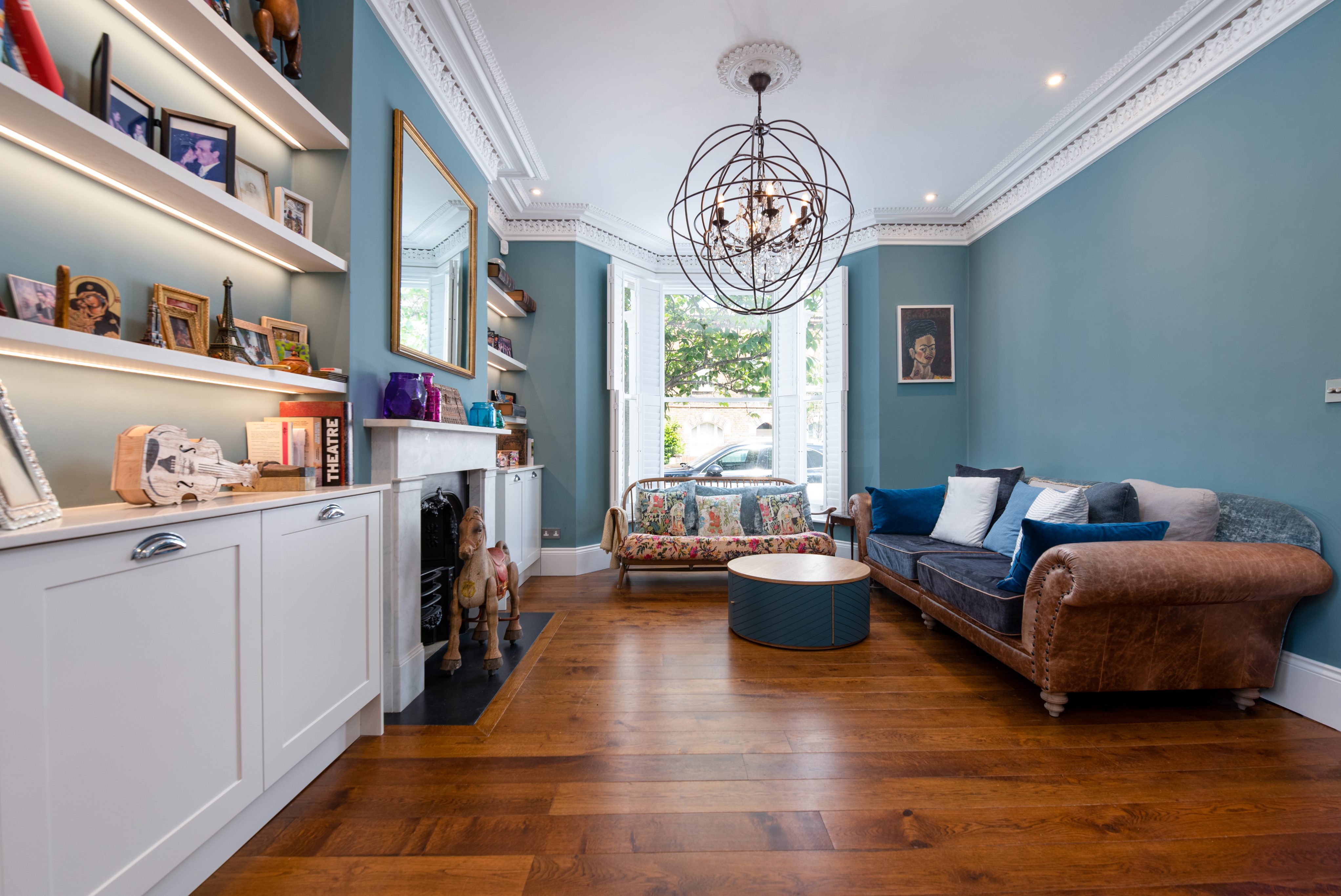 Bright and stylish living room featuring a mix of modern and traditional decor. The room showcases a comfortable sofa, a unique circular coffee table, and a decorative fireplace. A large mirror reflects natural light, enhancing the spacious feel. An Arch KBB team member is present, along with a dog, adding warmth to the inviting atmosphere.