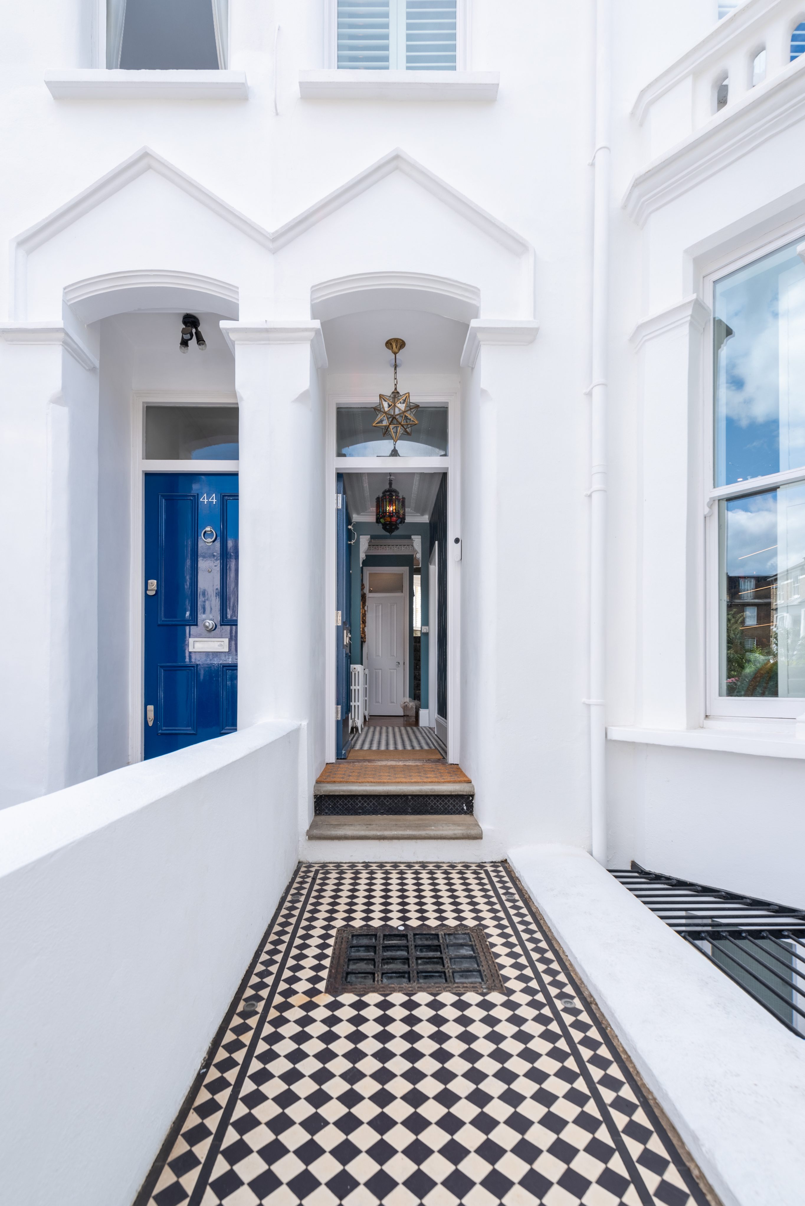 Entrance of a stylish home featuring a blue front door, patterned floor tiles, and a decorative light fixture. An Arch KBB team member stands at the entrance, welcoming visitors.