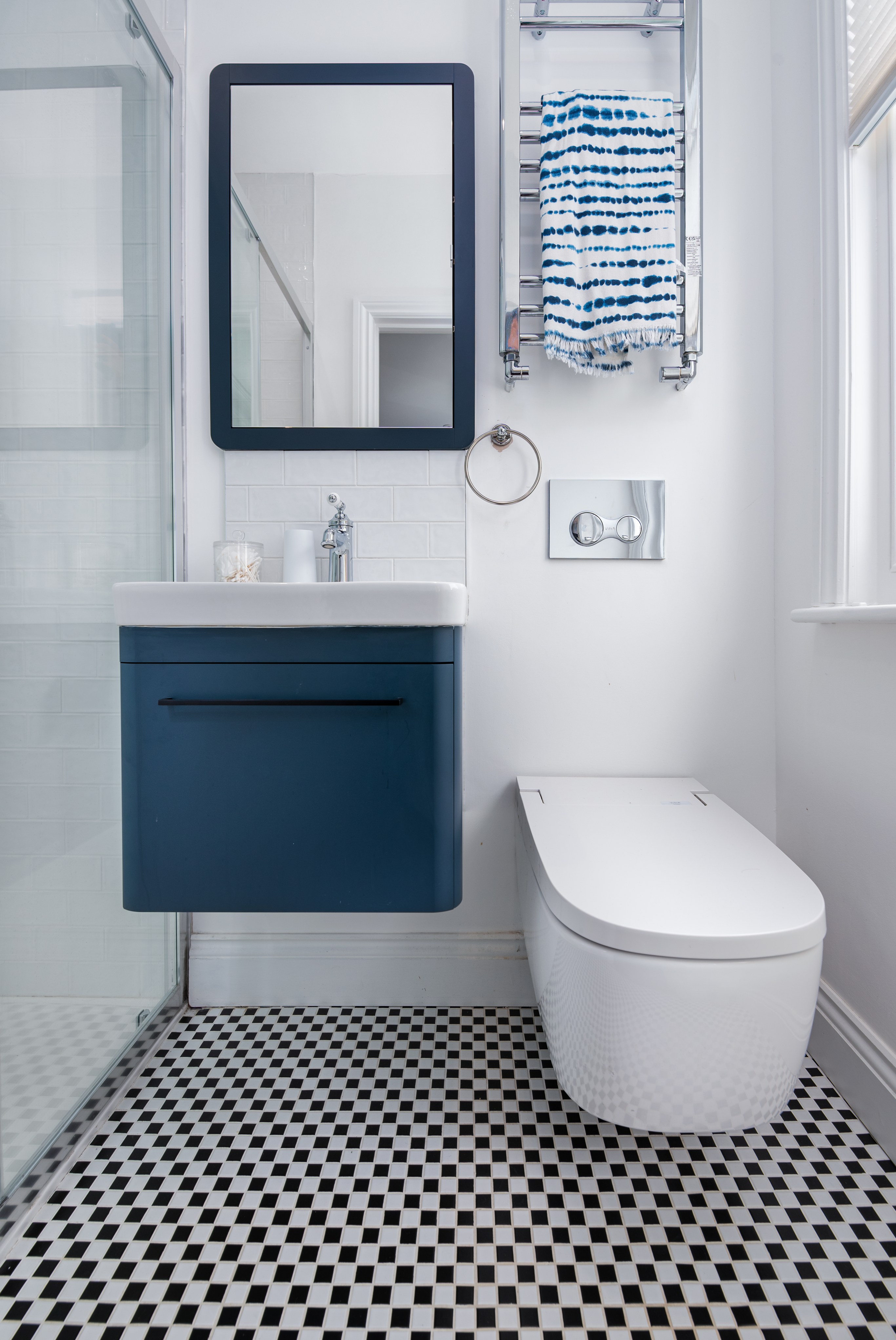 Modern bathroom featuring a wall-mounted vanity unit in navy blue, a sleek white toilet, and a large mirror. The space is bright with natural light, showcasing contemporary design elements and stylish fixtures. An Arch KBB team member is present, adding to the design expertise in the setting.