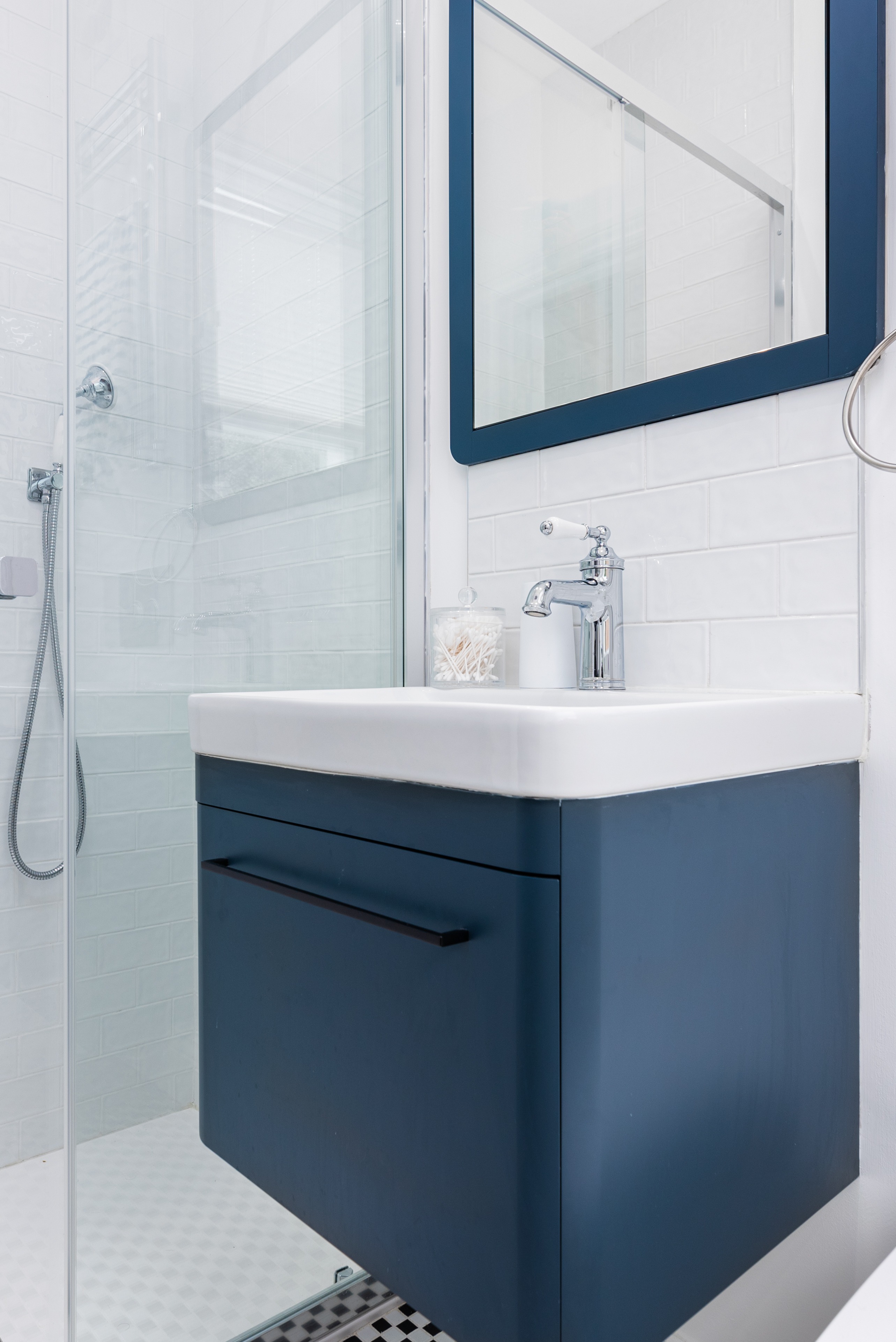 Modern bathroom design featuring a sleek blue vanity unit with a white countertop, a stylish basin tap, and a mirror with a blue frame. A glass shower enclosure is visible in the background, enhancing the contemporary aesthetic. Arch KBB team member present, showcasing a well-organised and stylish bathroom space.