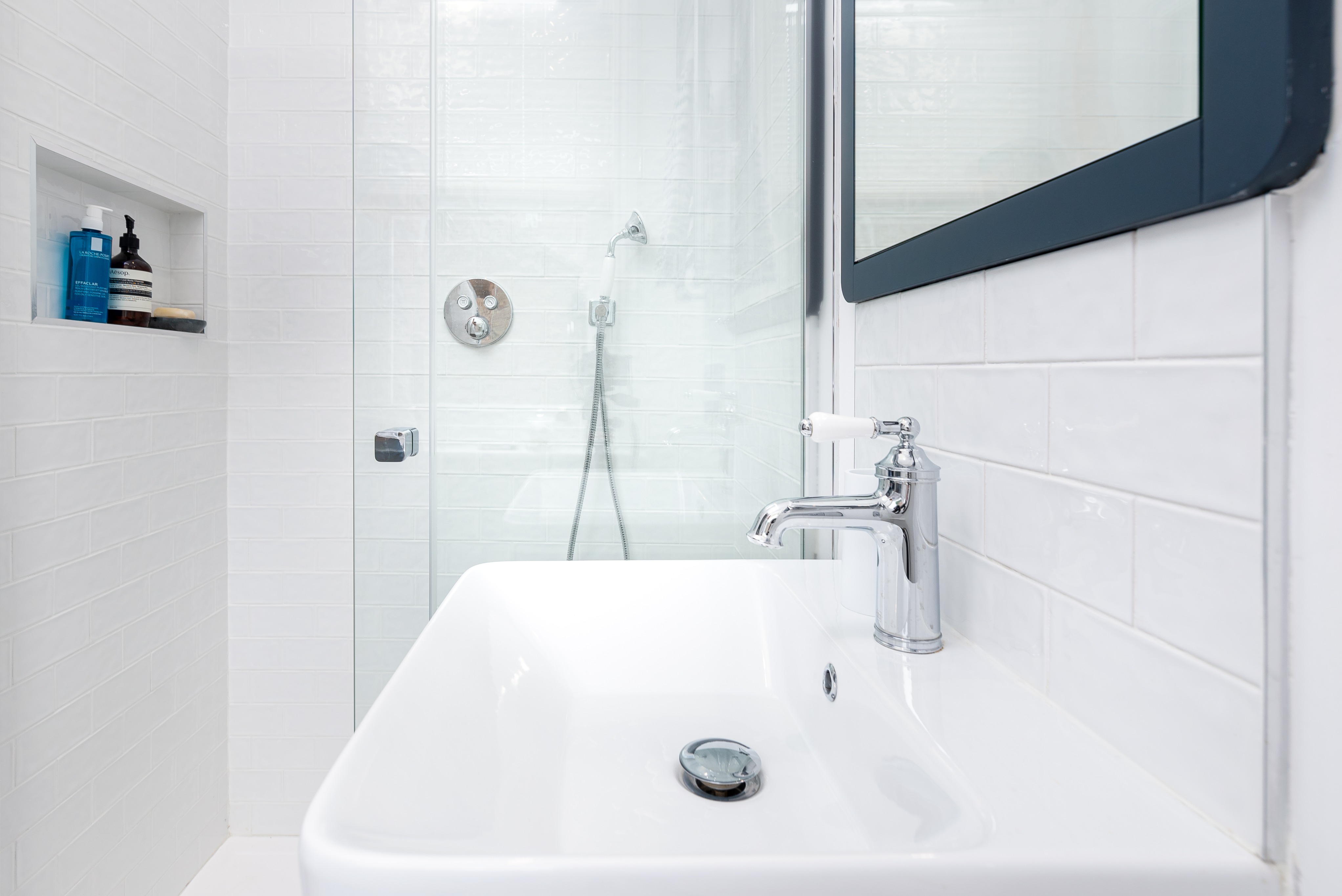 Modern bathroom featuring a stylish sink with a chrome tap, a glass shower enclosure, and sleek white tiles. An Arch KBB team member is present, showcasing the contemporary design and functionality of the space.