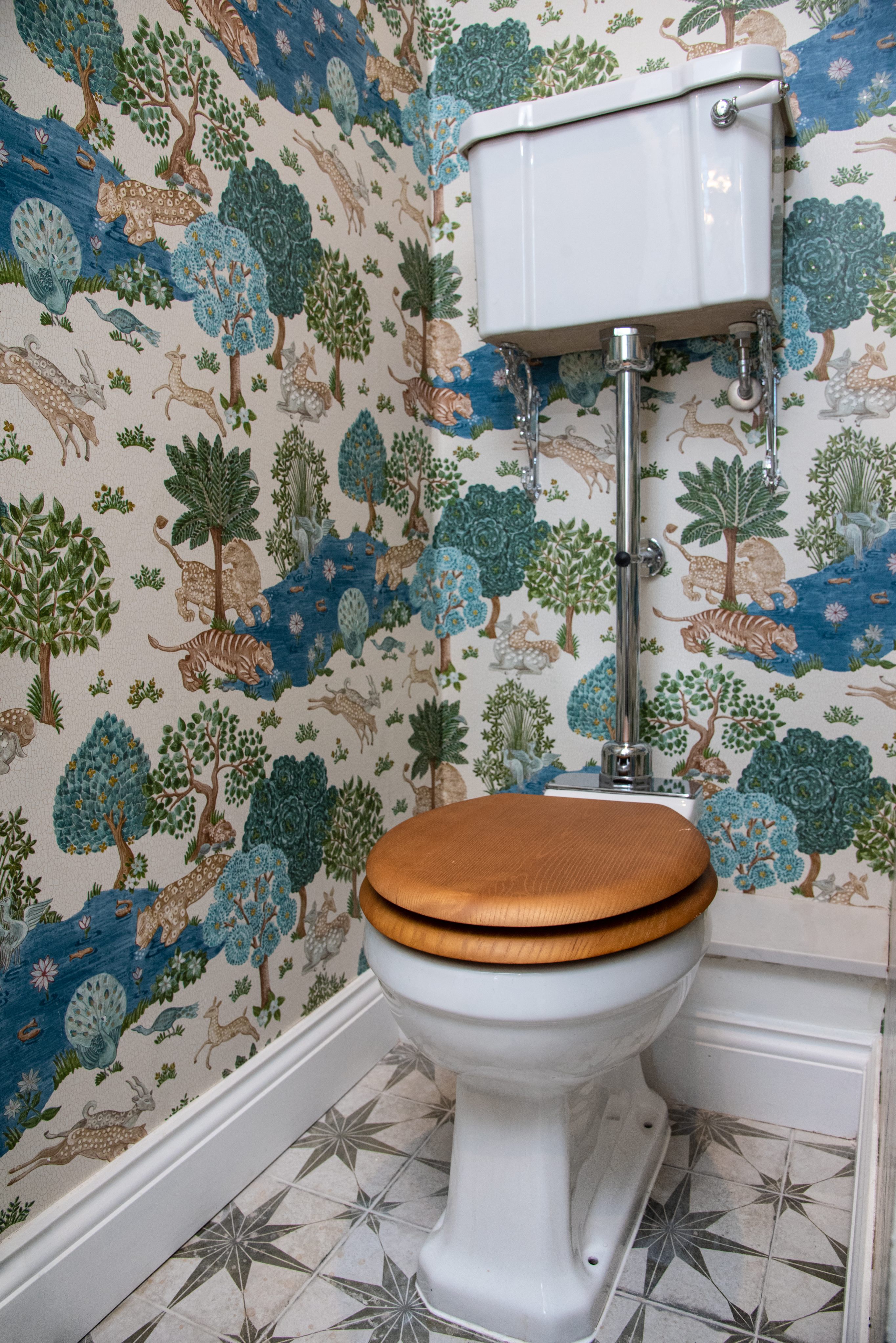 Alt text: A stylish bathroom featuring a wooden toilet seat and intricate wallpaper depicting a vibrant forest scene with animals and foliage. An Arch KBB team member is present, contributing to the design aesthetic.