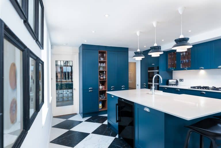 Modern kitchen design featuring blue cabinetry, a large white island with a sink, pendant lighting, and black-and-white chequered flooring.