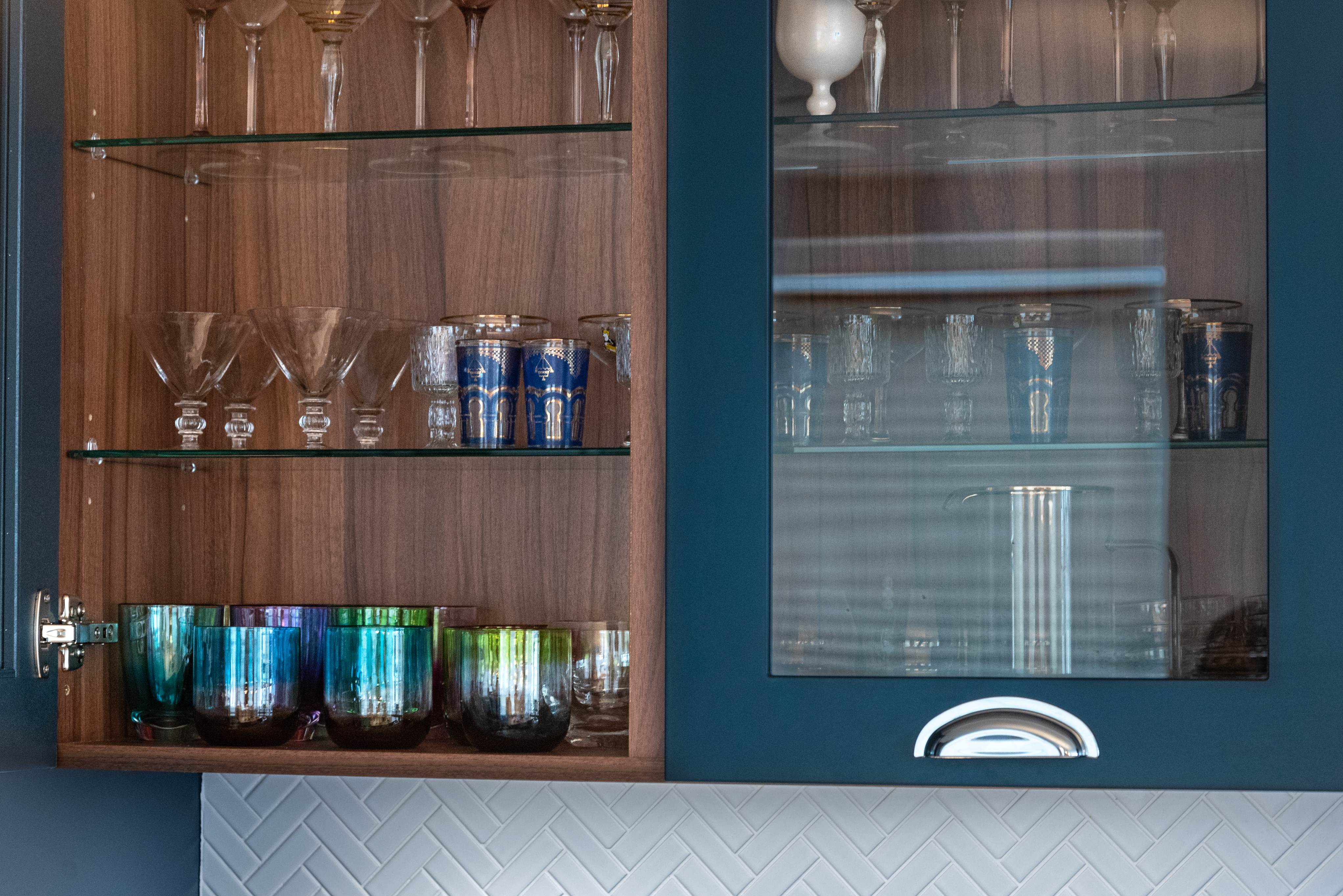 Interior shot of a kitchen cabinet showcasing a variety of glassware, including elegant wine glasses, colourful tumblers, and decorative items, highlighting the stylish design by an Arch KBB team member.