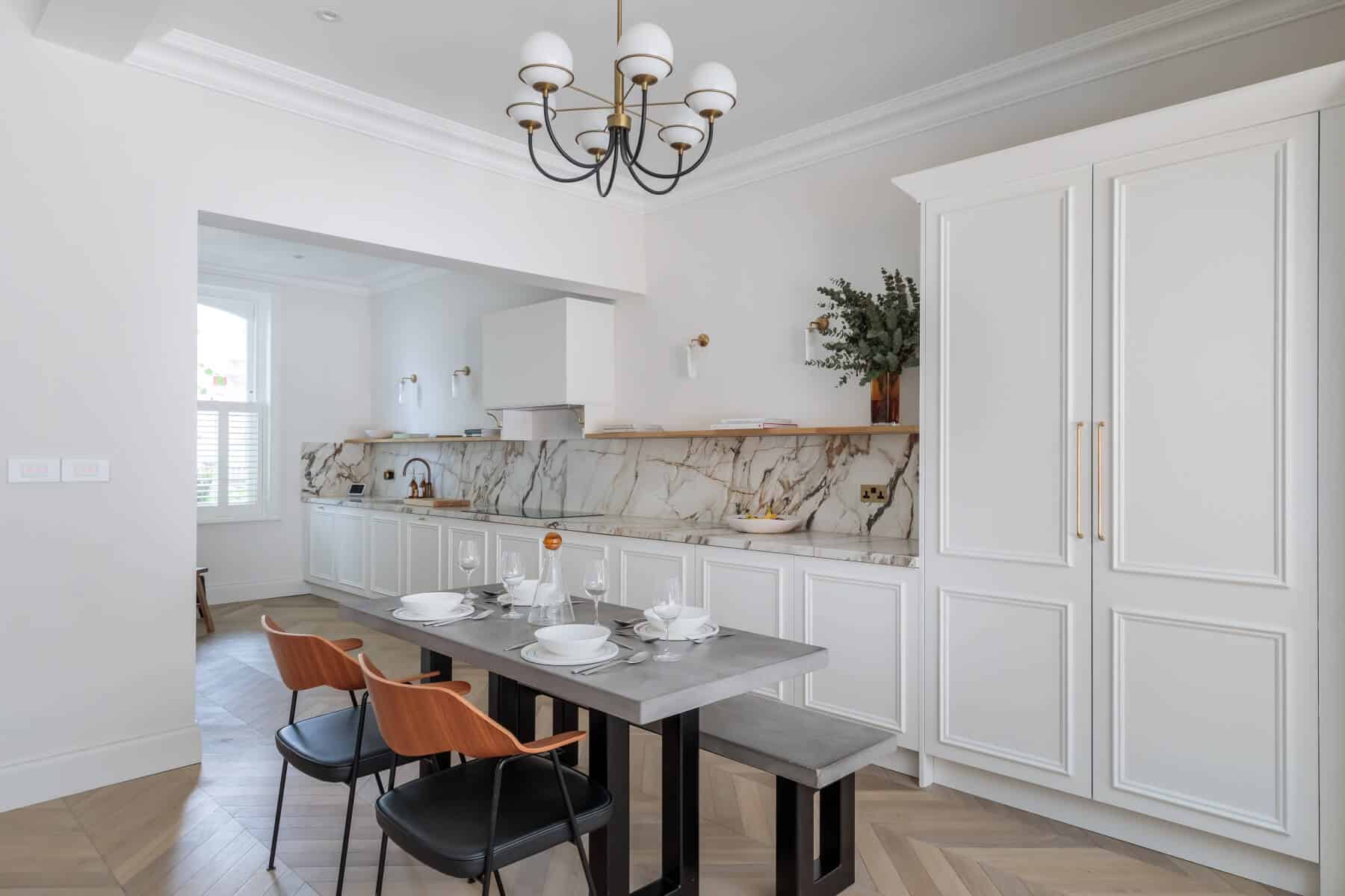 Modern kitchen interior featuring a stylish design with a marble backsplash, white cabinetry, and a contemporary dining table set for a meal. An Arch KBB team member is present, adding a personal touch to the elegant space. The room is well-lit, showcasing a blend of functionality and aesthetics.