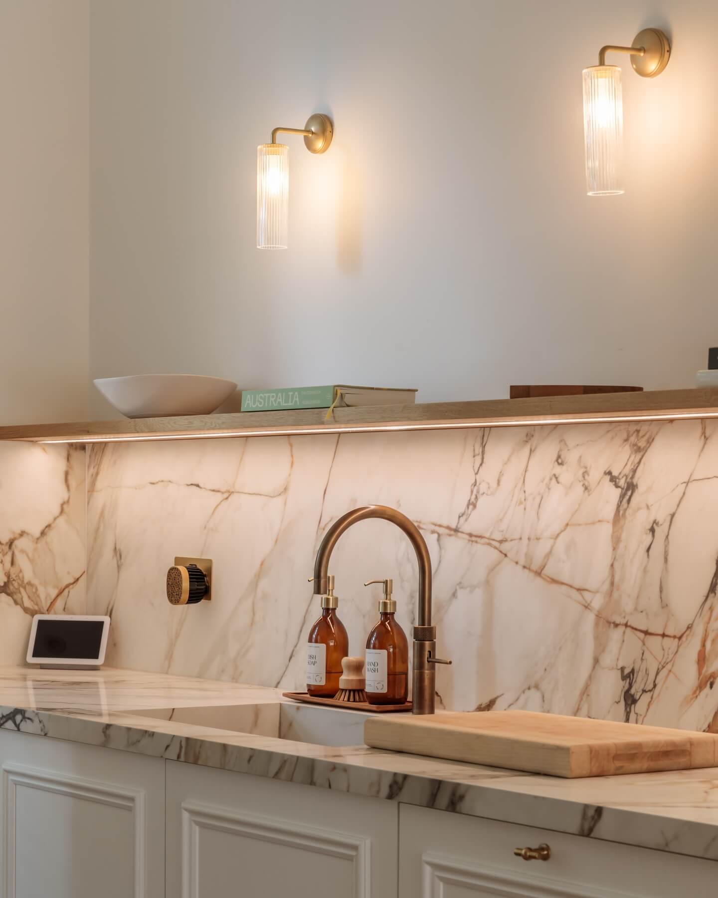 Modern kitchen design featuring elegant marble backsplash, stylish tapware, and decorative bottles. An Arch KBB team member is present, showcasing the sophisticated aesthetic and functionality of the space.