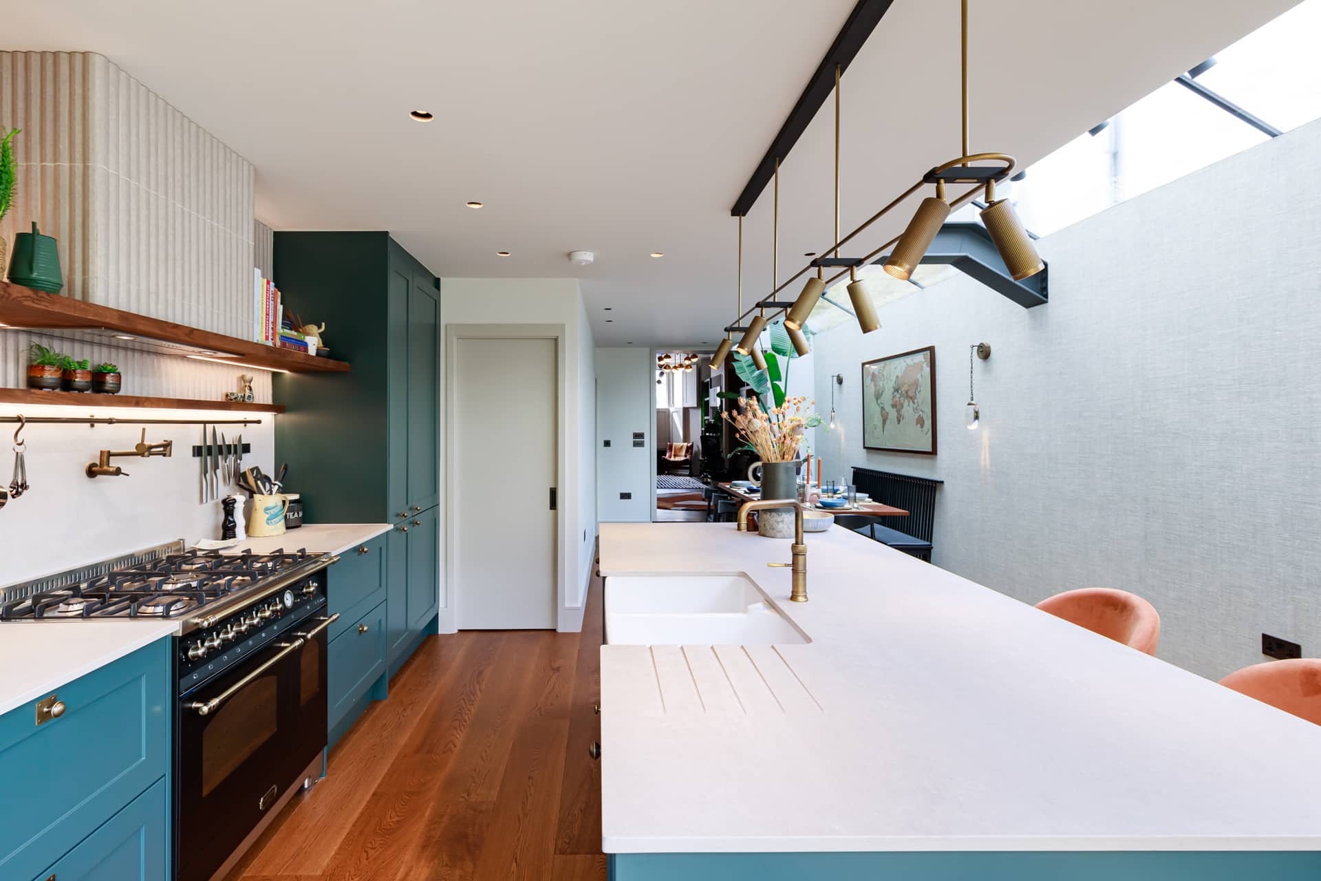 Modern kitchen featuring a stylish blue cabinetry, a large white countertop, and a gas stove. The space is illuminated by pendant lights and showcases an open layout with a dining area visible in the background. An Arch KBB team member is present, enhancing the vibrant atmosphere of this contemporary kitchen design.